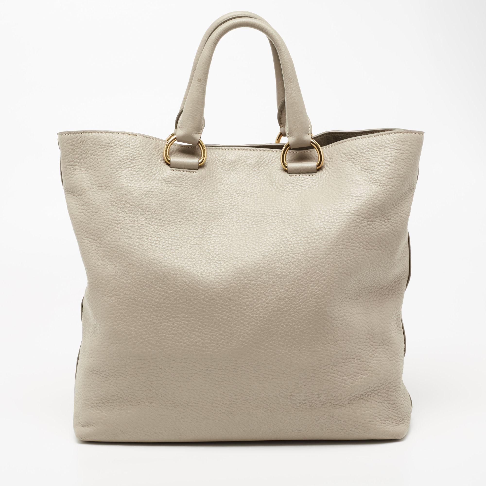 This Shopper tote from the House of Prada is great for everyday use. It is made from grey Vitello Daino leather, which is embellished with gold-tone hardware. It showcases dual handles and is provided with a nylon-lined interior. This Prada tote