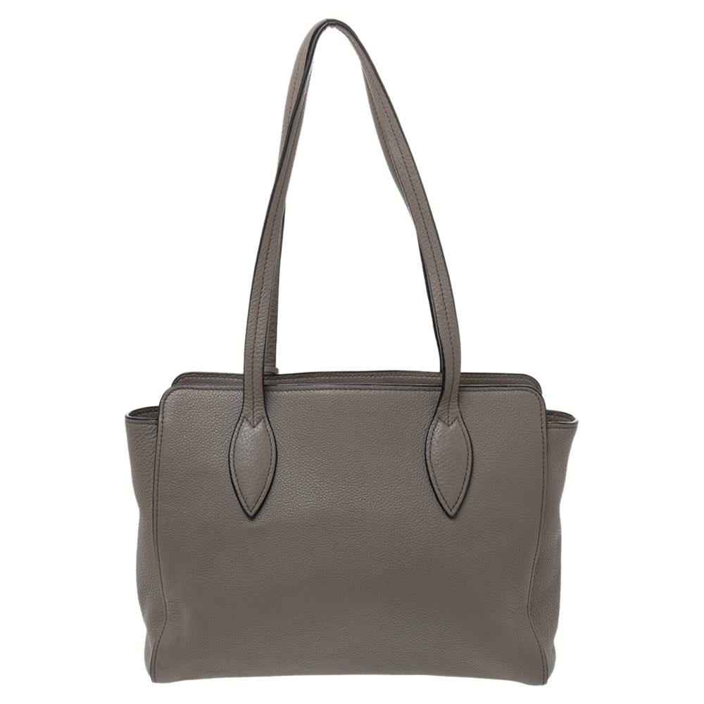 Featuring dual top handles and the brand label on the front, this Prada tote exudes just the right amount of sophistication. The tote opens to a nylon-leather lined interior that houses ample space for your essentials. This piece is definitely an