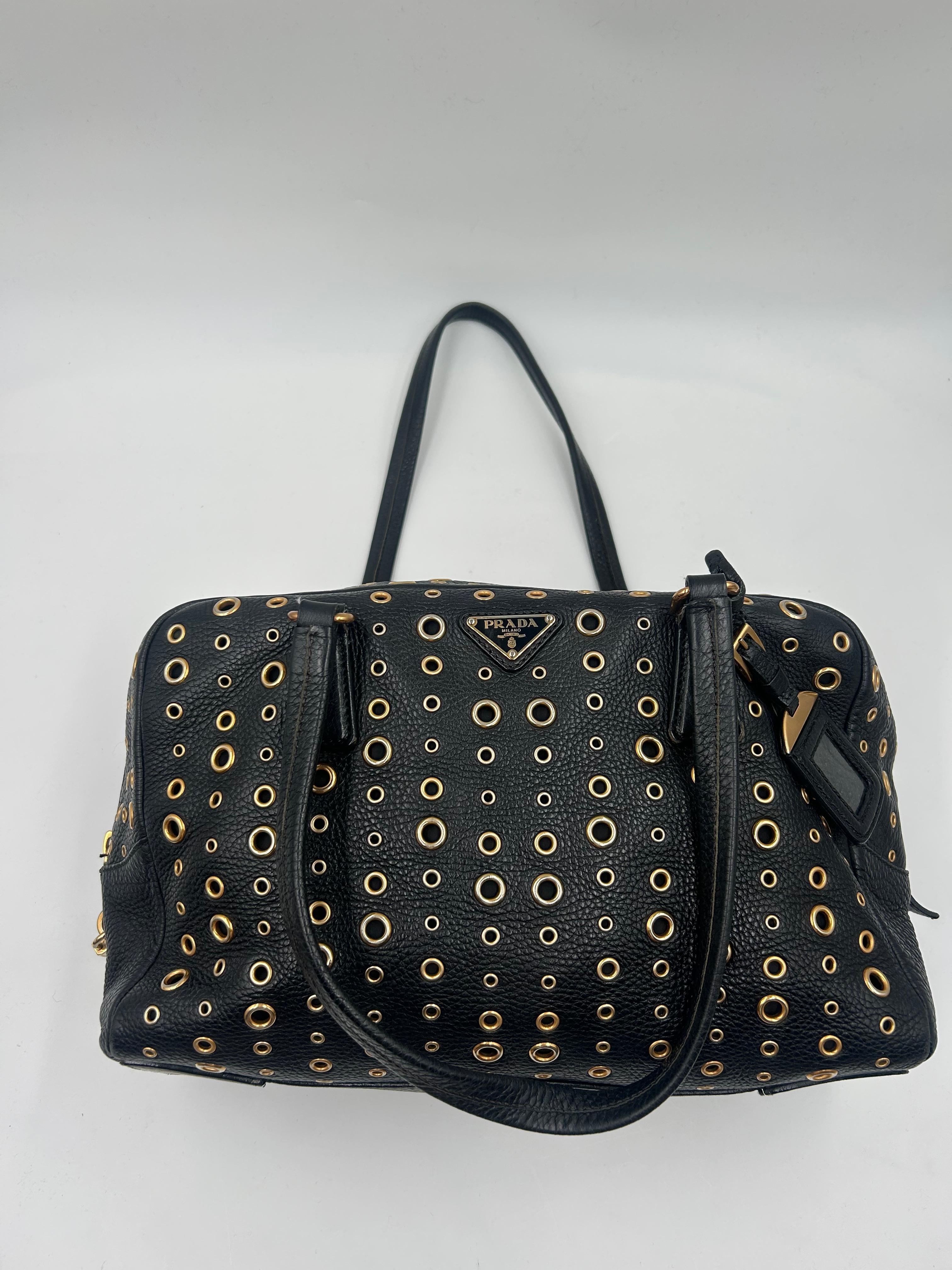 Audacieux et contemporain, ce sac Grommet Bauletto de Prada est confectionné en cuir lisse et orné d'œillets dorés. Doté de deux poignées supérieures, d'une silhouette structurée et du logo Prada, il offre un intérieur spacieux et une sophistication