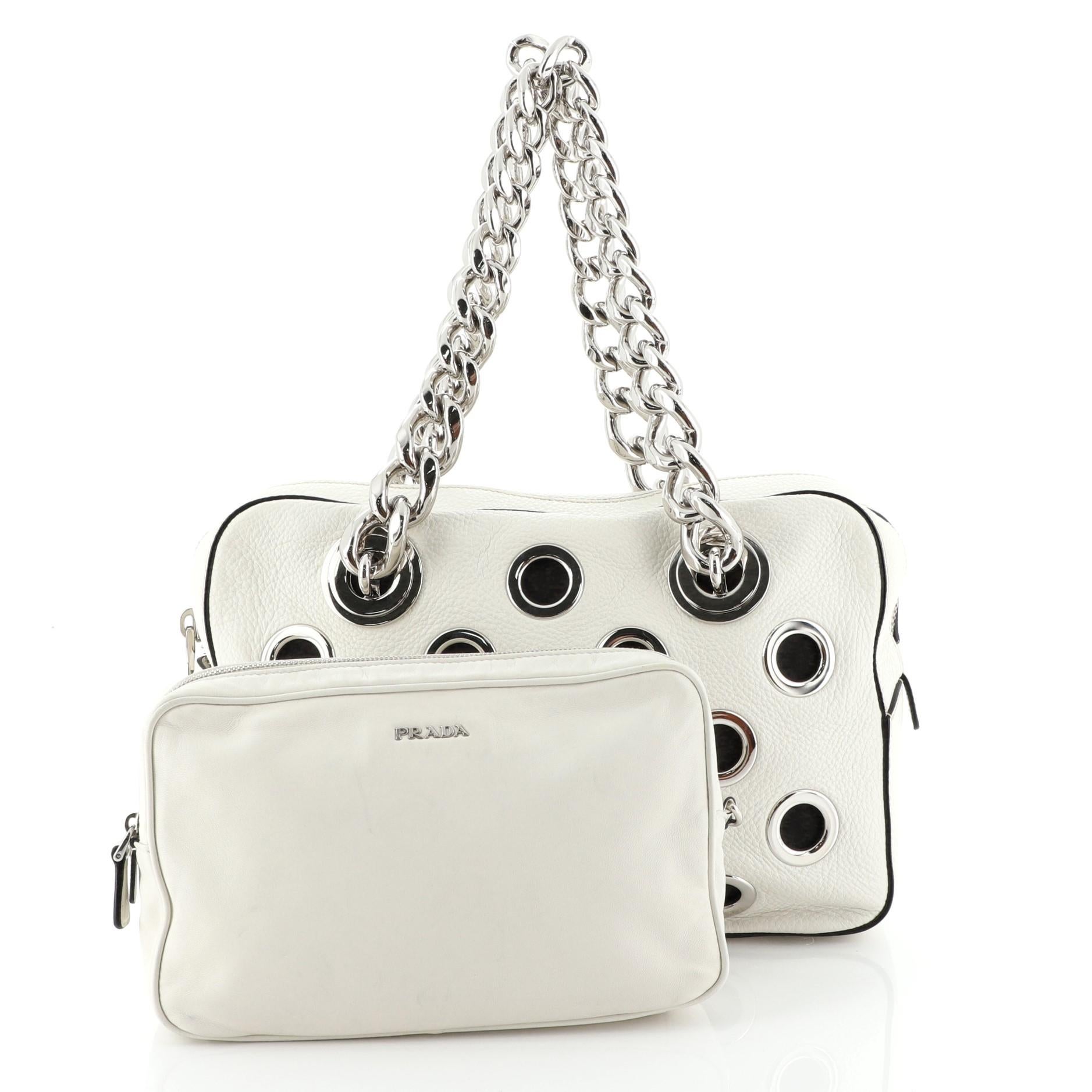 This Prada Grommet Chain Shoulder Bag Vitello Daino Medium, crafted from white vitello daino leather, features dual chain straps, large grommets detailing all throughout, protective base studs and silver-tone hardware. Its zip closure opens to a