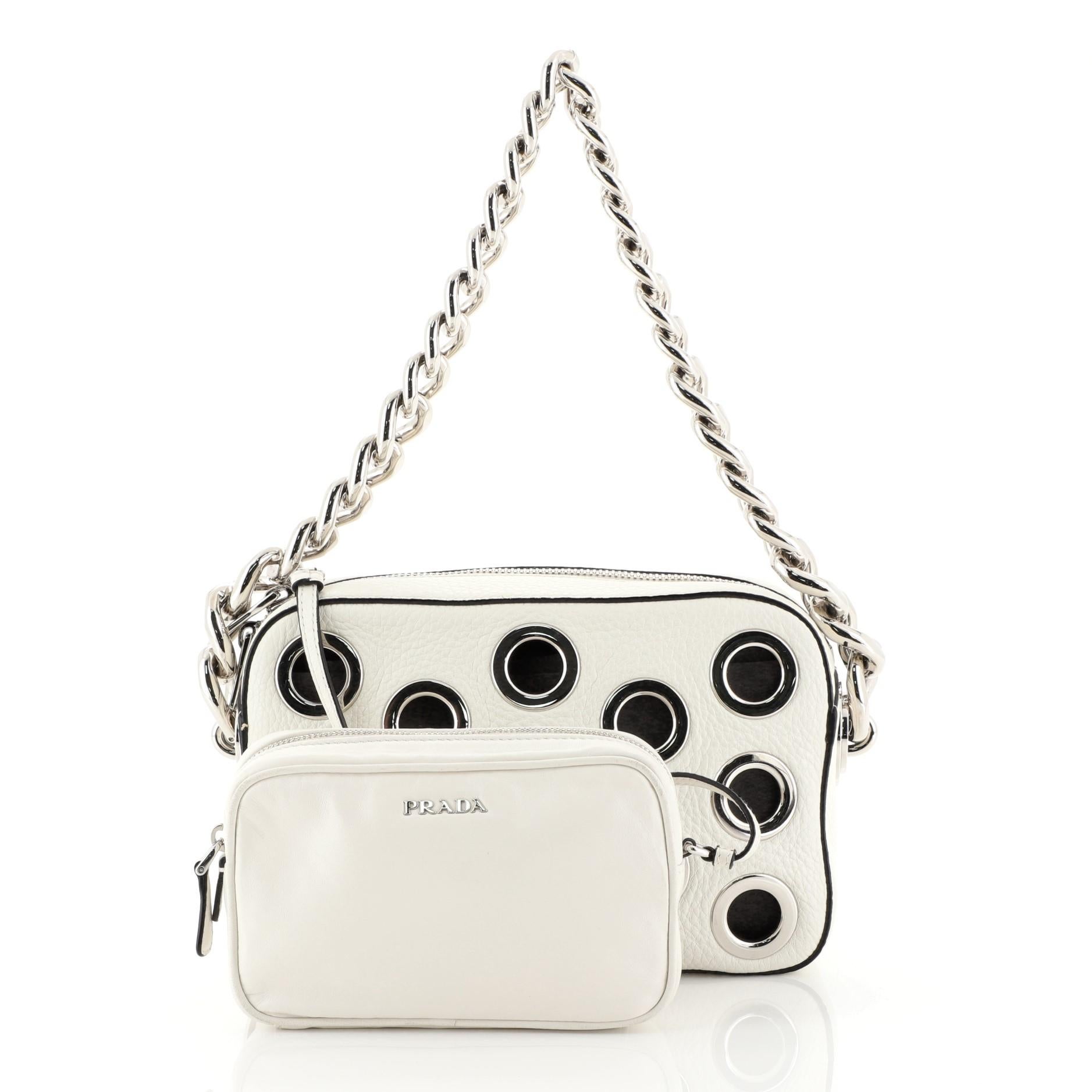 This Prada Grommet Chain Shoulder Bag Vitello Daino Small, crafted from white vitello daino leather, features chain link straps, large grommets detailing all throughout, and silver-tone hardware. Its zip closure opens to a white leather interior.