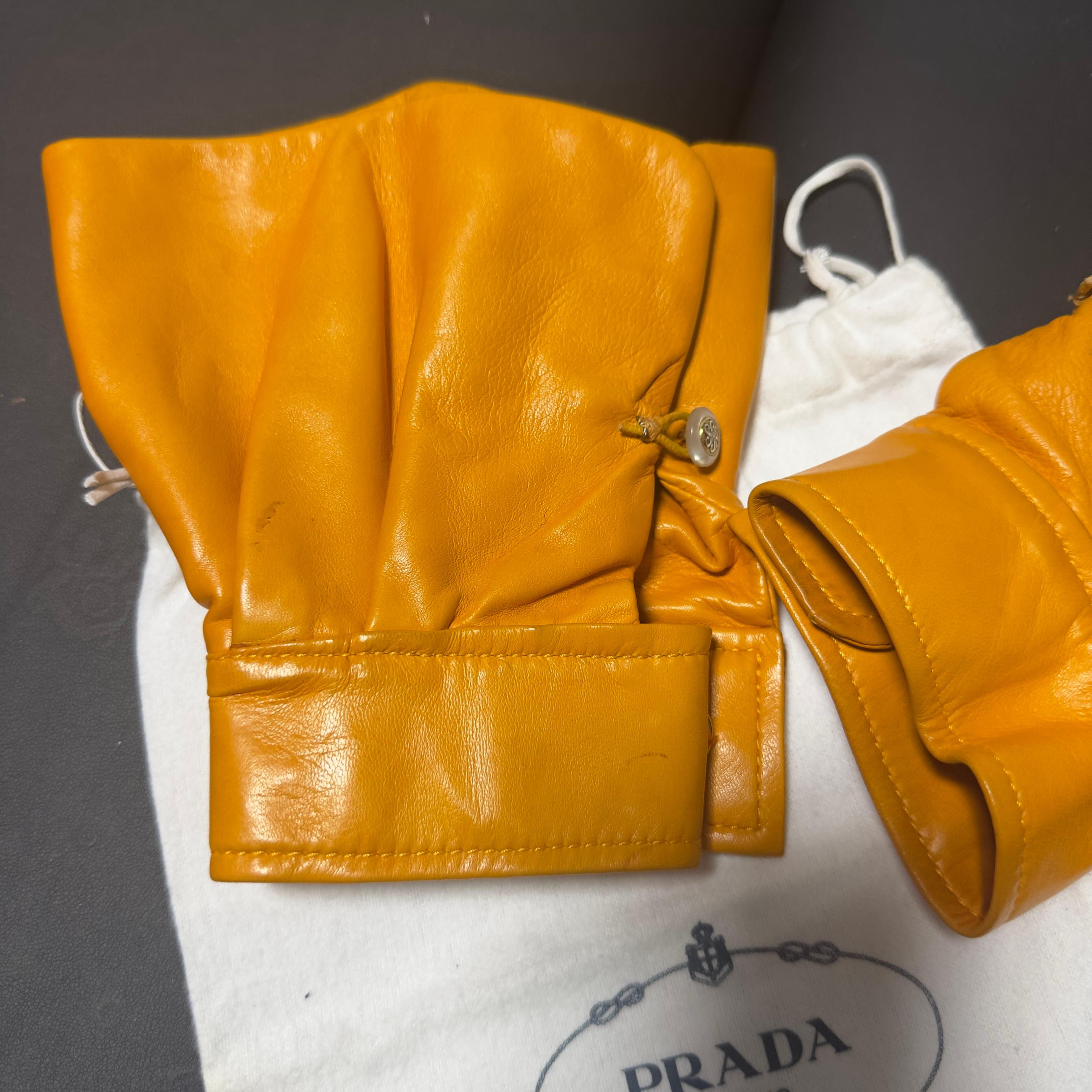 Gants couture Prada rares en cuir souple moutarde/jaune safran, présentant un design sculptural avec de larges fronces et une manchette structurée. Le modèle se distingue par sa fermeture avec un bouton iconique en métal gravé et un détail