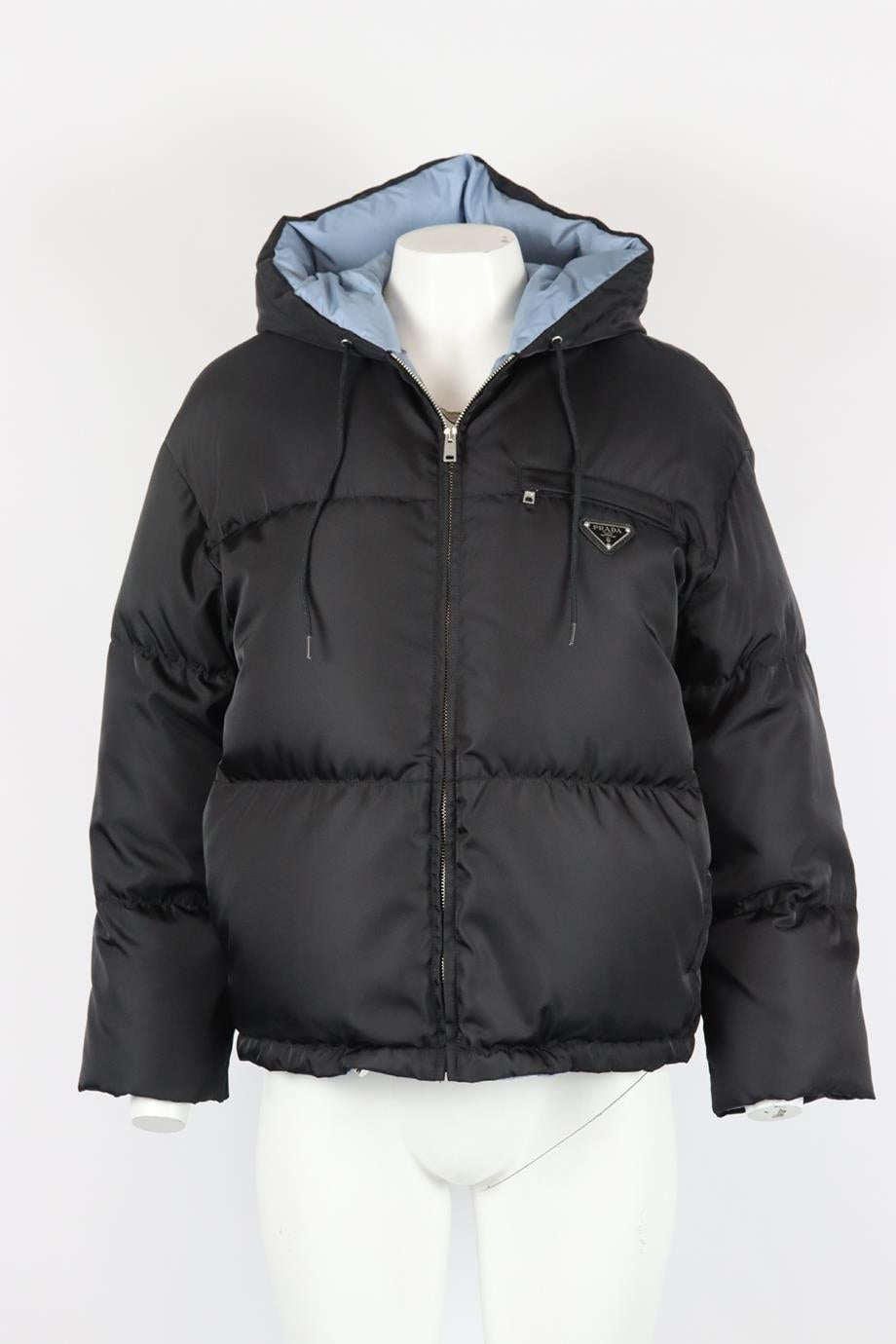 Prada hooded logo appliquéd quilted shell down jacket. Black and blue. Long sleeve, crewneck. Zip fastening at front. 100% Recycled polyamide; lining: 100% polyamide; padding: white goose down and feathers (90% down); filler bag: 100% polyester.