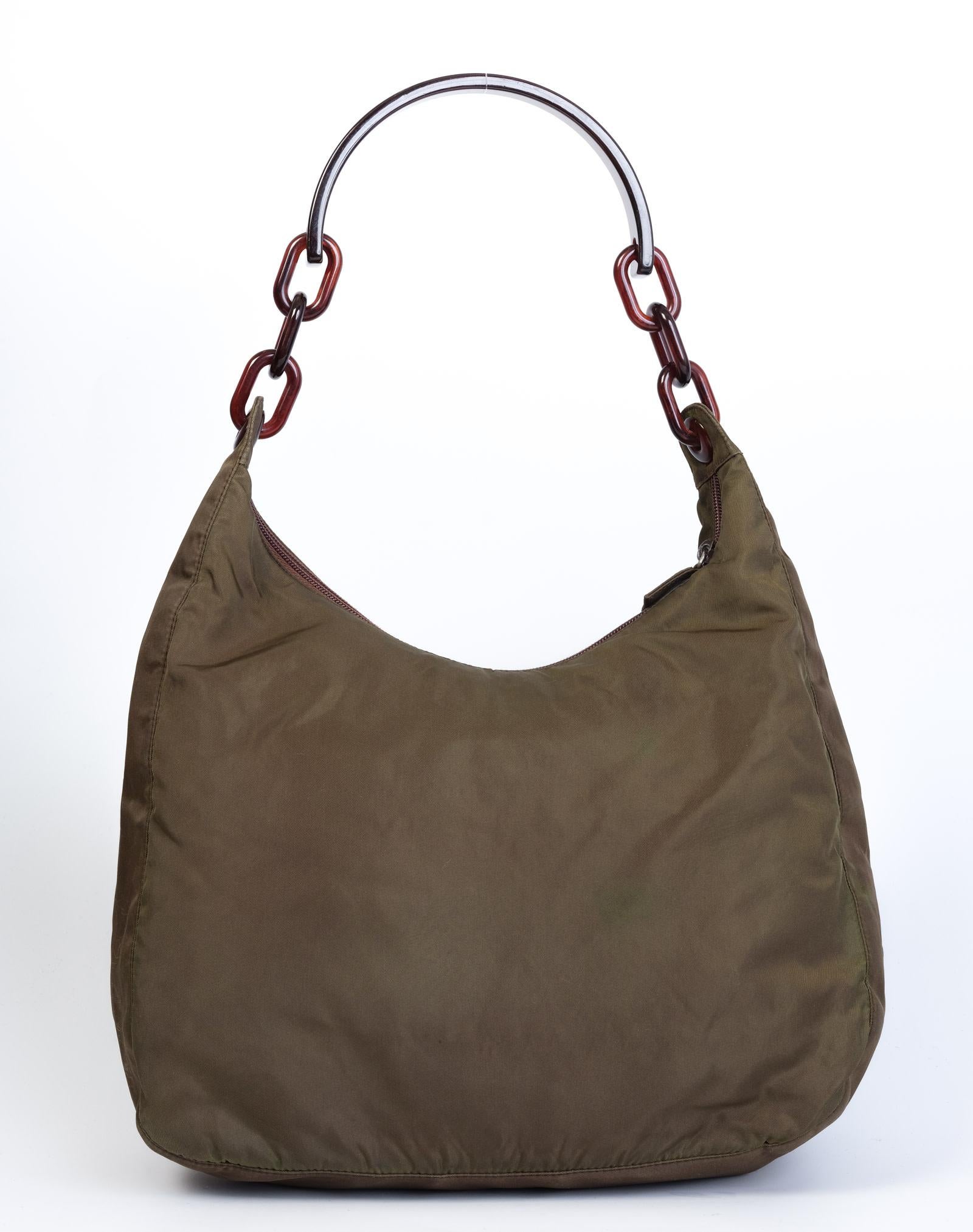 This bag is made with khaki nylon and features a tortoise shell chain handle, top zip closure and one main compartment with additional zip pockets.

COLOR: Green
MATERIAL: Nylon
ITEM CODE: N
MEASURES: H 11” x L 9” x D 4”
DROP: 10”
CONDITION: Good -