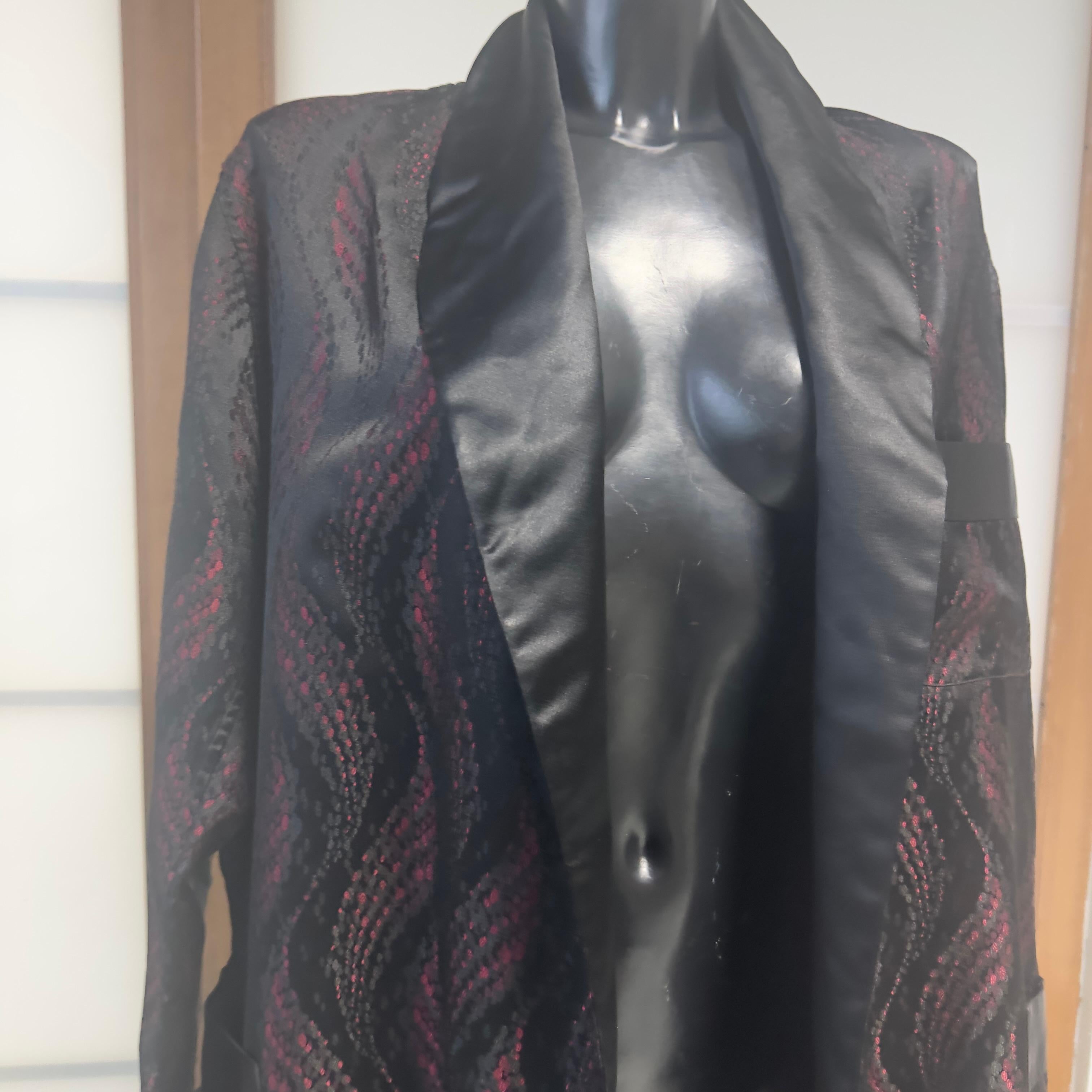 Cet extraordinaire kimono Prada allie l'élégance du brocart à une allure nocturne et sophistiquée. Réalisé dans un jacquard riche en nuances de noir et de bordeaux, ce vêtement présente un motif ondulant qui court sur la surface comme un relief