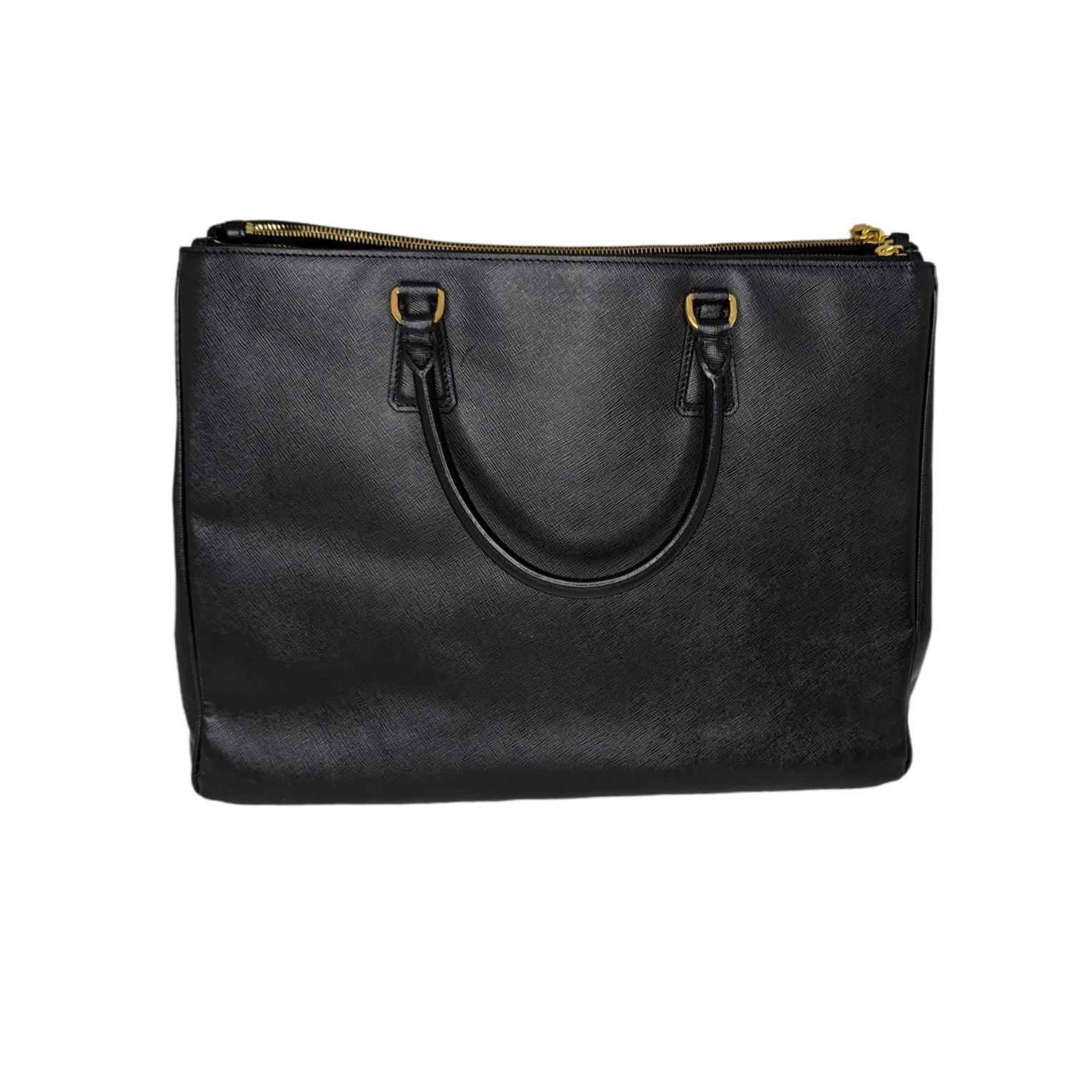This chic tote is crafted of Prada signature Saffiano cross-grain leather in black. The tote features rolled leather top handles and polished gold links. The top is open to a black fabric interior with two full length zippered pockets, a zipper
