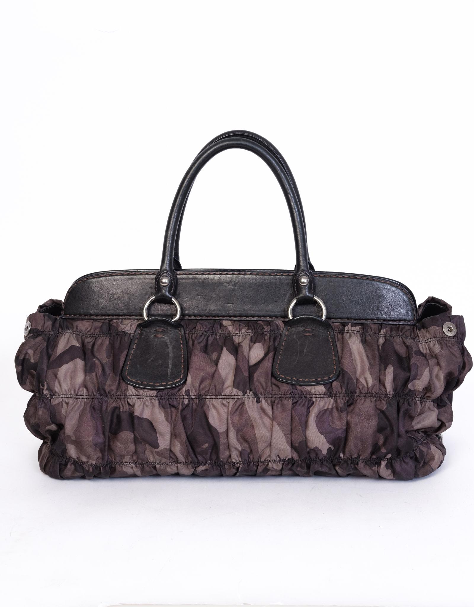 This camo Gaufre Prada bag features leather trim, silver tone hardware, single interior wall pocket with zip closure, interior patch pockets and top magnetic snap closure.  

COLOR: Camo
MATERIAL: Nylon/ Leather
ITEM CODE: 7
MEASURES: H 10” x L 17”