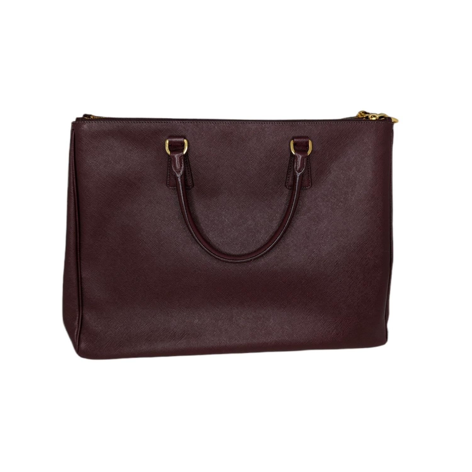 This chic tote is crafted of Prada signature Saffiano cross-grain leather in wine. The tote features rolled leather top handles and polished gold links. The top is open to a wine fabric interior with two full length zippered pockets, a zipper pocket