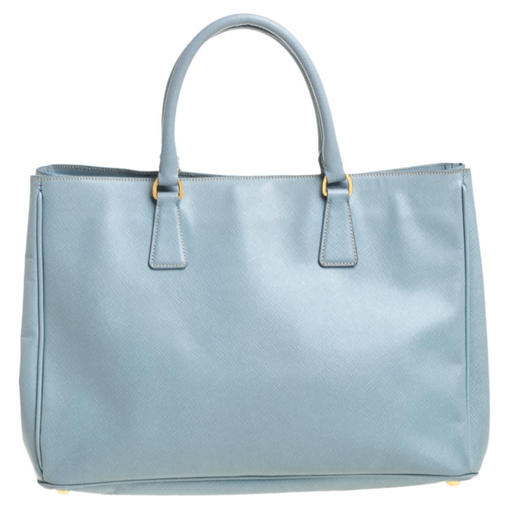 Grand in shape and design, this tote by Prada will be a loved addition to your closet. It has been crafted using Saffiano leather and styled minimally with gold-tone hardware. It comes with two top handles and a perfectly-sized main compartment. The