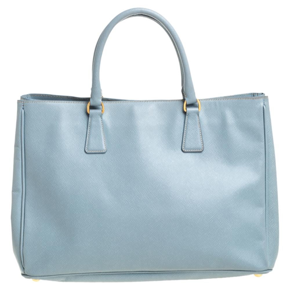 Großartig in Form und Design, wird diese Tasche von Prada eine beliebte Ergänzung für Ihren Kleiderschrank sein. Sie wurde aus Saffiano-Leder gefertigt und minimalistisch mit goldfarbenen Beschlägen gestaltet. Sie verfügt über zwei Griffe an der