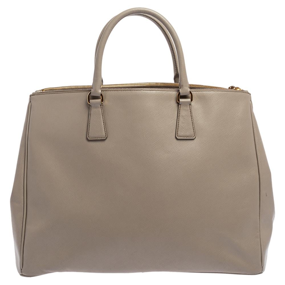 Feminine in shape and grand on design, this Double Zip tote by Prada will be a loved addition to your closet. It has been crafted from Saffiano Lux leather and styled minimally with gold-tone hardware. It comes with two top handles, two zip