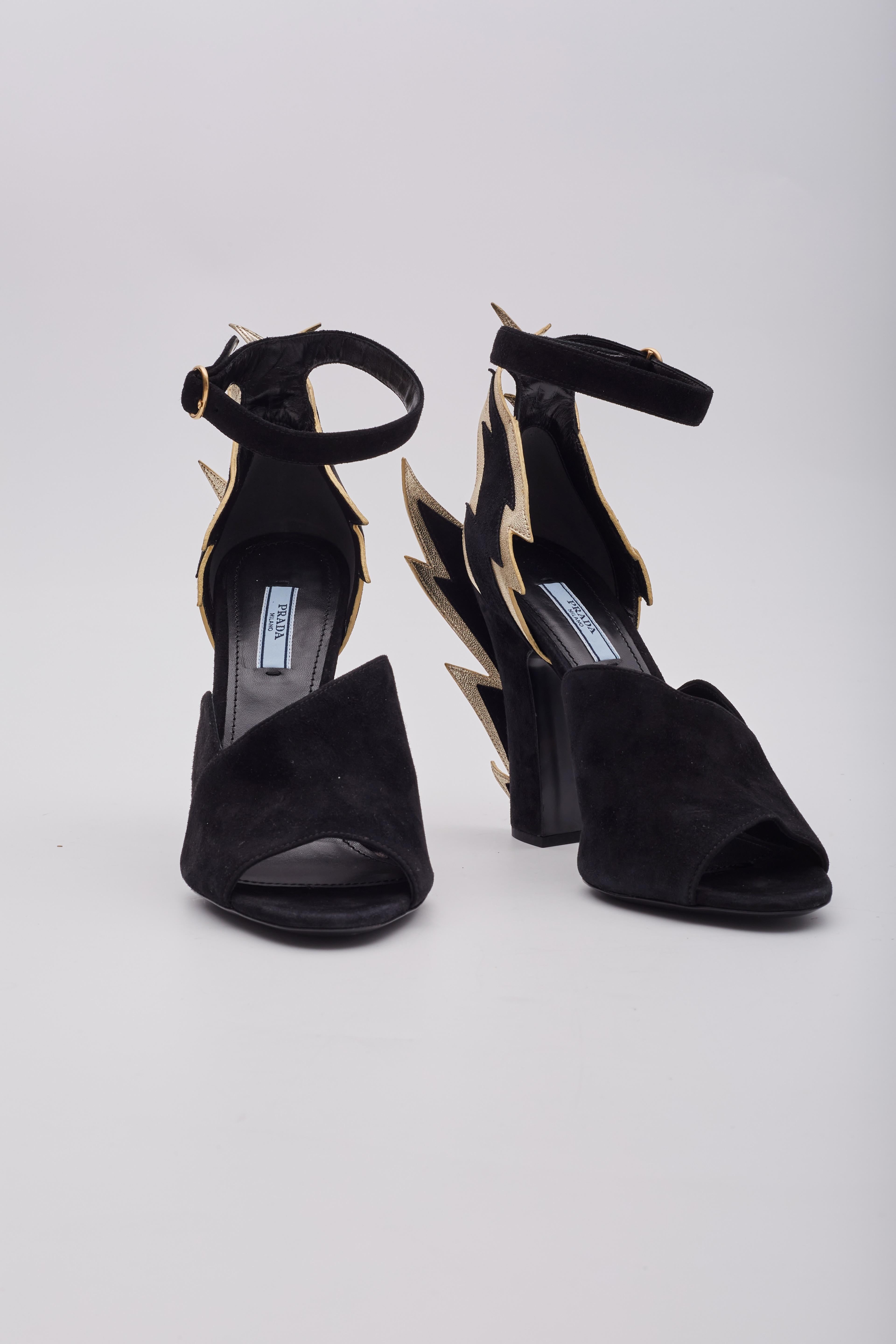 Featuring black suede construction, the Lightning bolt on the heel with gold leather trim, ankle strap closure, peep toe and a chunky heel.Estimated Retail Price: US $1250.

Color: Black
Material: Suede
Designer: Miuccia
Year/Collection: 2019