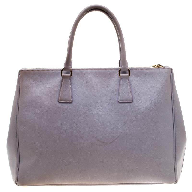 Feminine in shape and grand on design, this Double Zip tote by Prada will be a loved addition to your closet. It has been crafted from Saffiano Lux leather and styled minimally with gold-tone hardware. It comes with two top handles, two zip