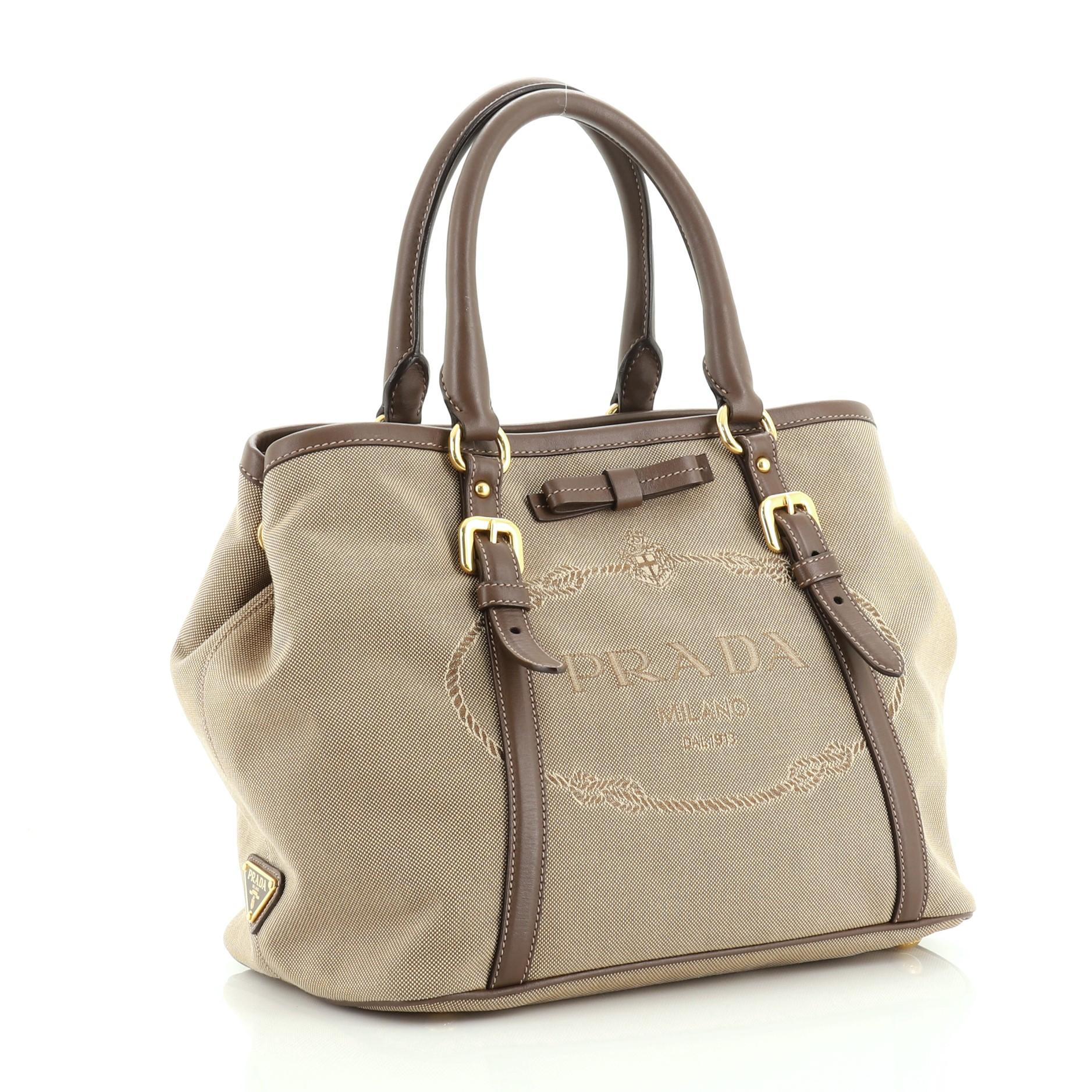 This Prada Logo Convertible Tote Canvas with Leather Medium, crafted from brown leather and canvas, features Prada logo at the front, dual rolled handles and gold tone hardware. It opens to a brown fabric interior with zip pocket. 

Estimated Retail