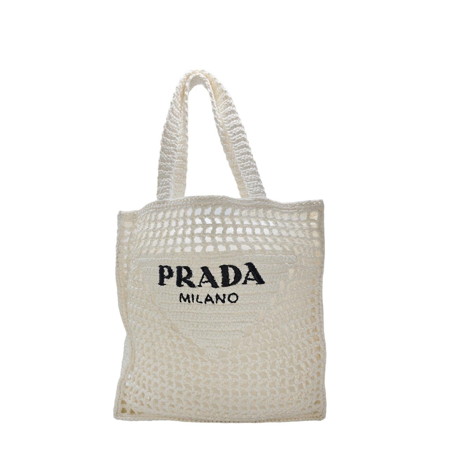The Prada embroidered Logo Crochet Raffia Tote with a soft, deconstructed design boasts a light and summery mood, perfect for carrying all your essentials. Crafted with white crocheted Raffia and dual handles, it offers effortless style and
