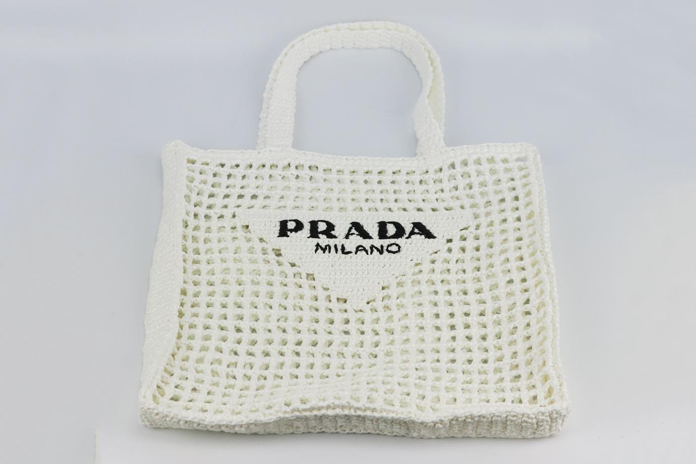 Prada logo embroidered raffia tote bag. Made from white cutout raffia with logo embroidery in black at the front. White and black. Open top. Comes with dustbag and authenticity card. Width: 14.5 in. Height: 15 in. Depth: 1.5 in. Handle Drop: 9 in
