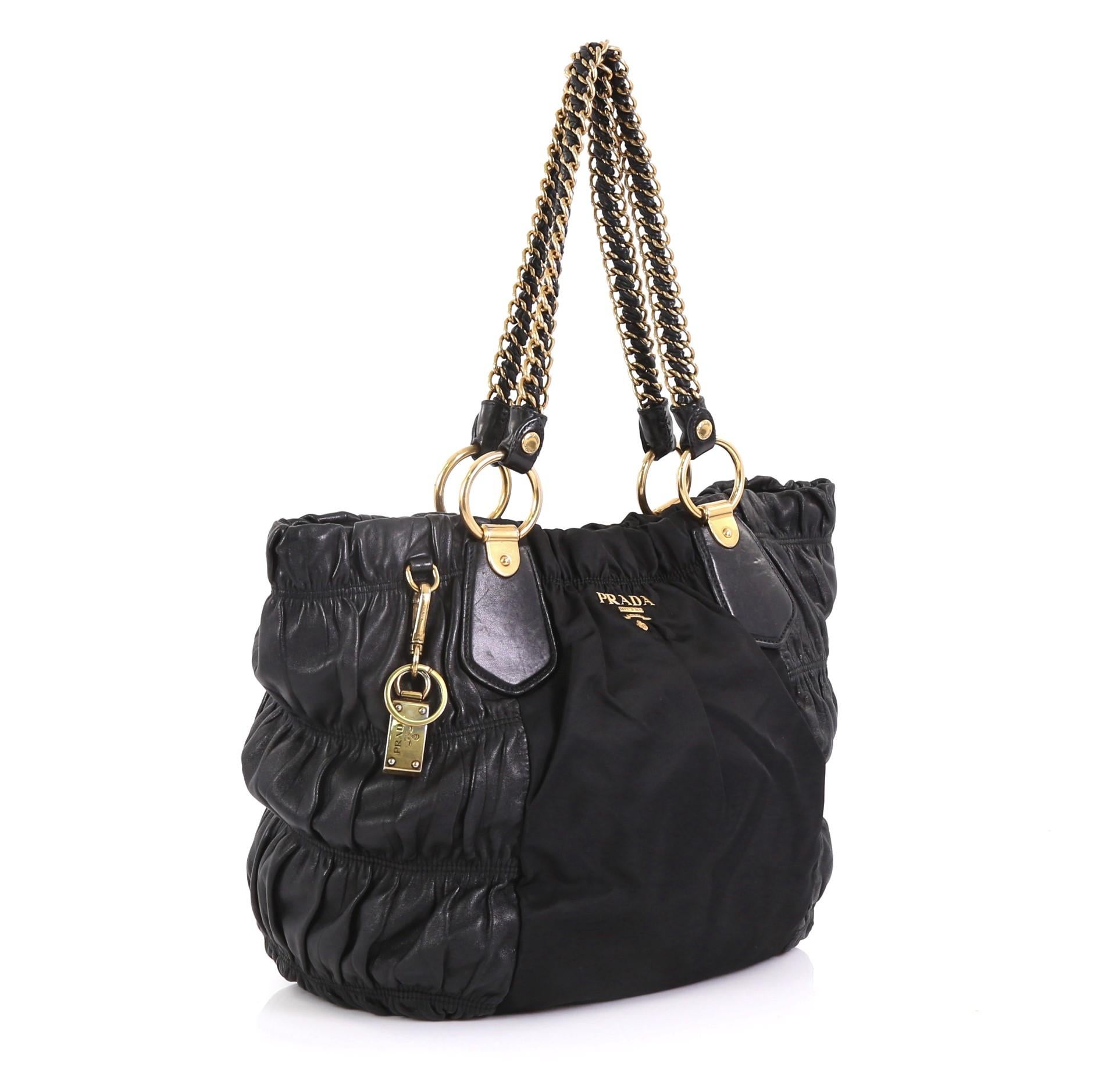 This Prada Lux Chain Strap Gaufre Tote Leather and Tessuto Large, crafted in black leather and tessuto, features dual woven-in leather chain straps, Prada logo and gold-tone hardware. Its snap button closure opens to a black fabric interior with zip