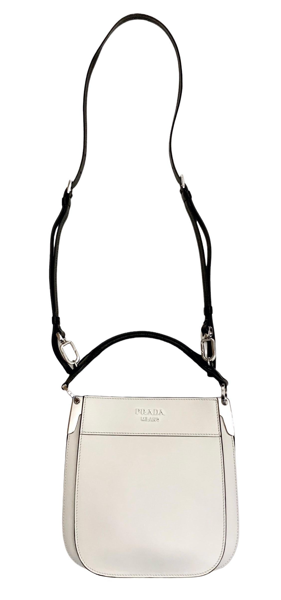 This pre-owned but perfect white Prada Margit leather cross body bag has been crafted from a very fine calfskin leather into a square box with a rounded base.
The upper closure is finished by double magnetic buttons. 
The bag features a black
