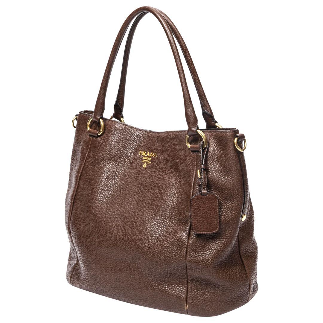 Prada's Medium Convertible Tote in brown grained calfskin shines with gold fittings, a logo jacquard interior lined with a zippered pocket, all held together by a magnetic snap.

SPECIFICS
Length: 13.8