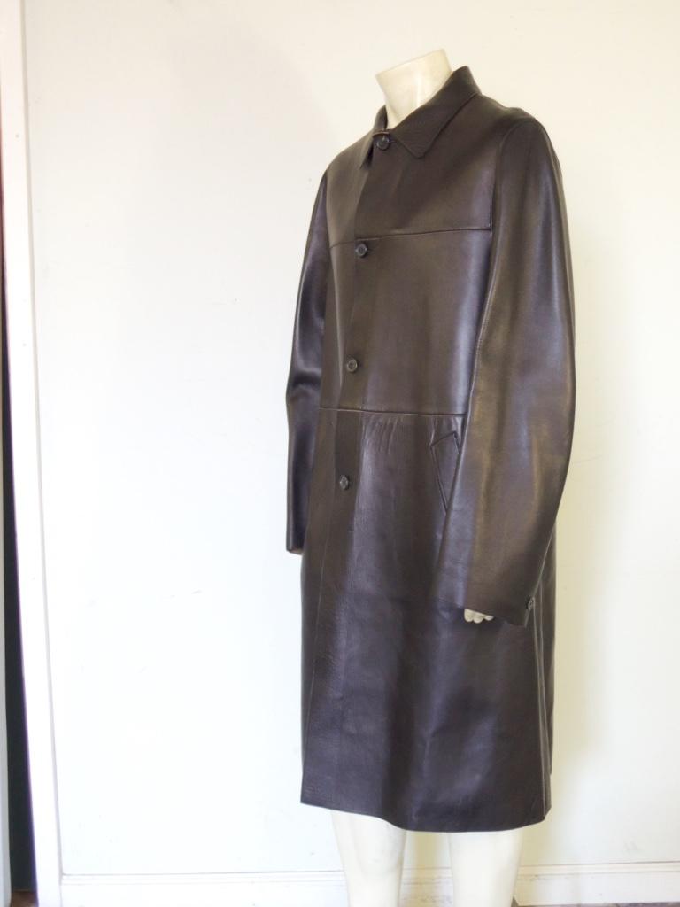 This is a men's Prada black leather trench coat with a 4-button front, Prada logo buttons, and two front slash pockets. One important note - this coat has what appears to be belt loops but there is no belt included with this coat. 

This piece is