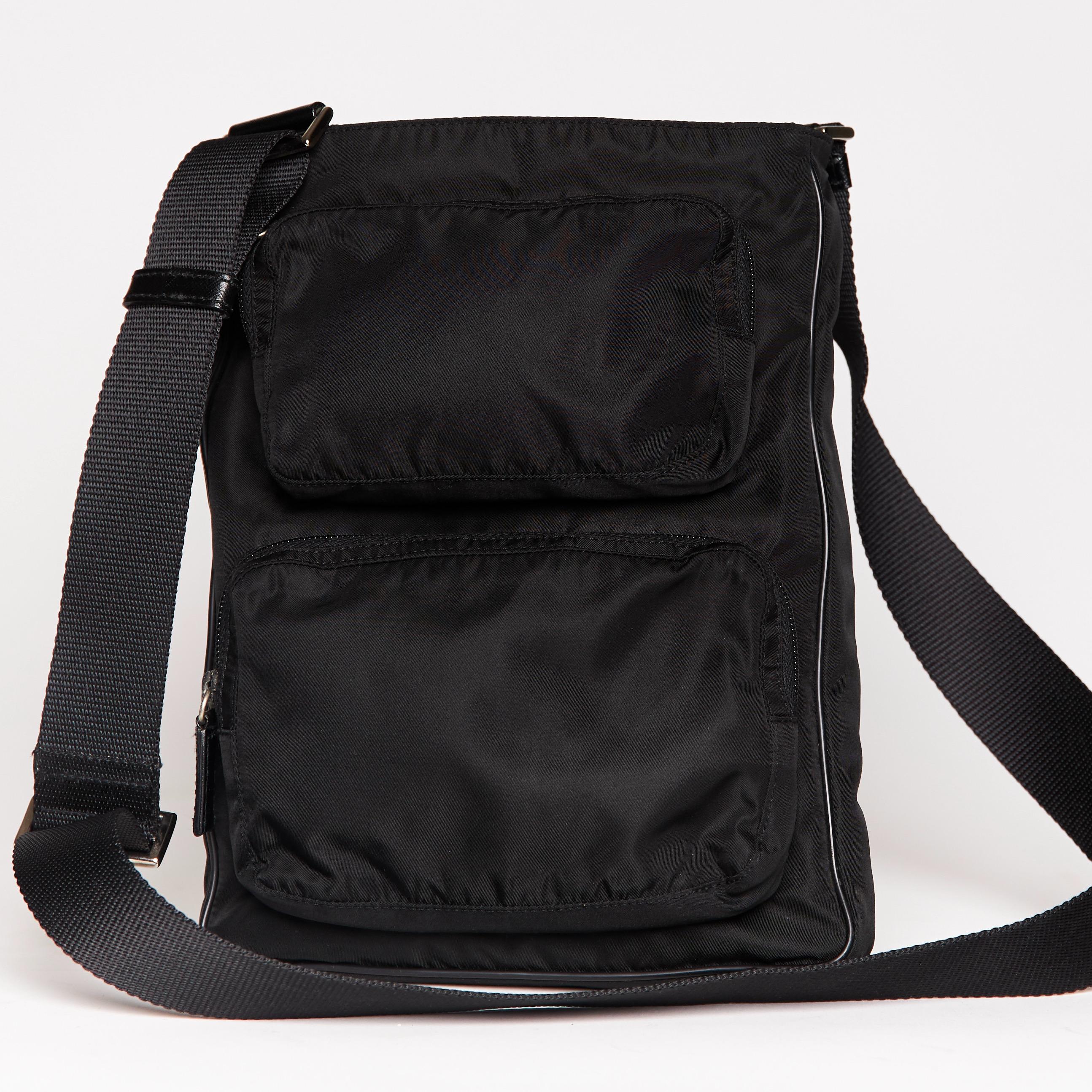 Diese Prada Tasche ist aus schwarzem Nylon mit Lederbesatz und -abschlüssen. Die Tasche hat einen langen schwarzen Schulterriemen aus gewebtem Stoff, zwei Reißverschlusstaschen auf der Vorderseite, einen Reißverschluss an der Oberseite und ein
