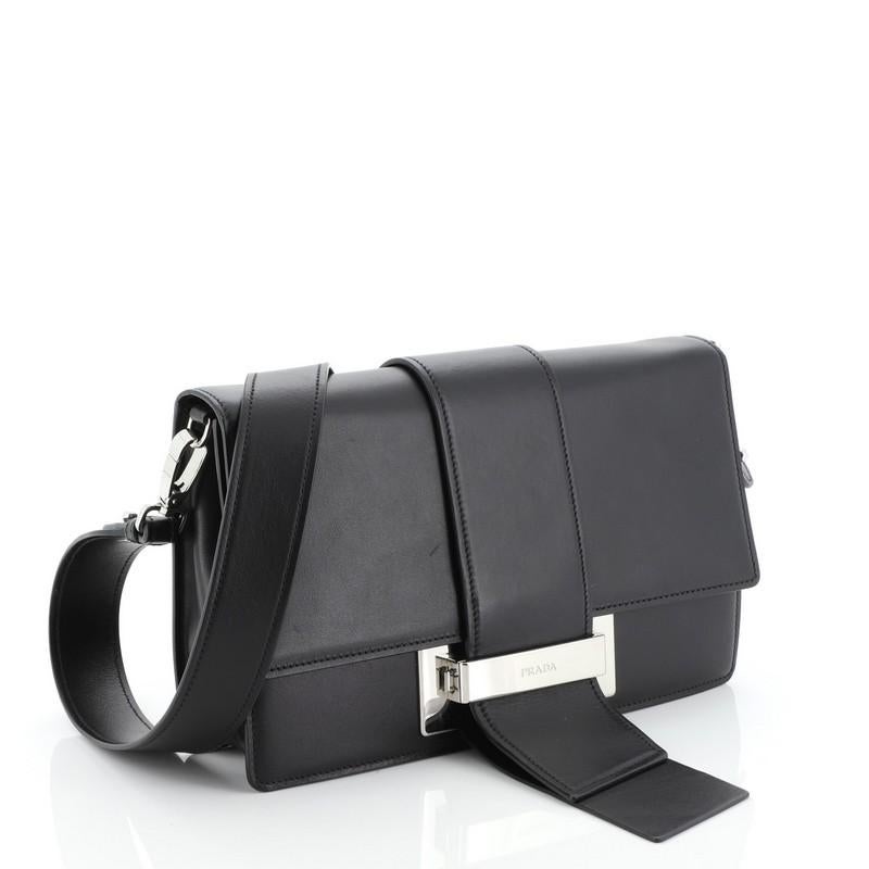 This Prada Metal Ribbon Shoulder Bag City Calfskin Medium, crafted in black leather, features removable shoulder strap, flap top with push-lock tab closure and silver-tone hardware. Its push-lock closure opens to a black fabric interior with zip
