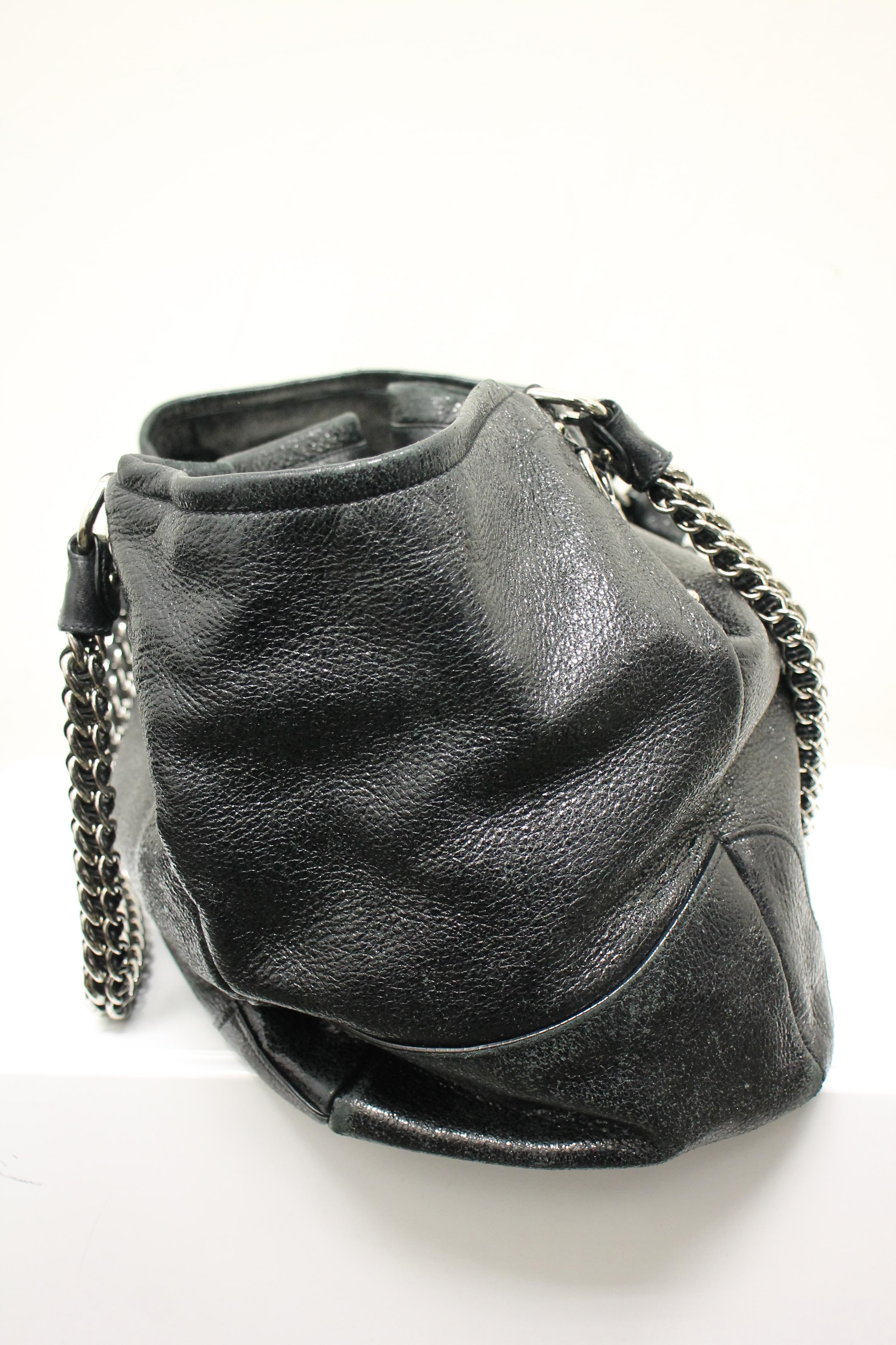 Black metallic sparkled leather. Silver-tone hardware. Magentic snap closure at top. Dual top heavy chain shoulder straps. Logo at front. Lined interior. One interior opened pocket. One interior zippered pocket.