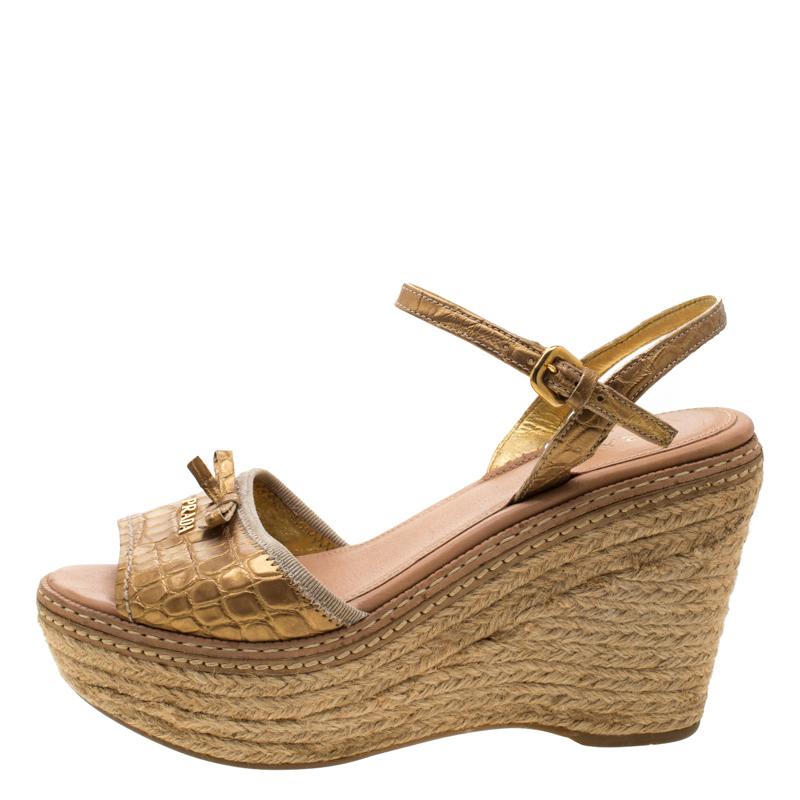 These beautiful croc-embossed leather sandals are a great option while choosing footwear for any occasion. Designed by Prada, these metallic gold sandals feature open toes, ankle fastening, and wedge heels for all-day comfort.

