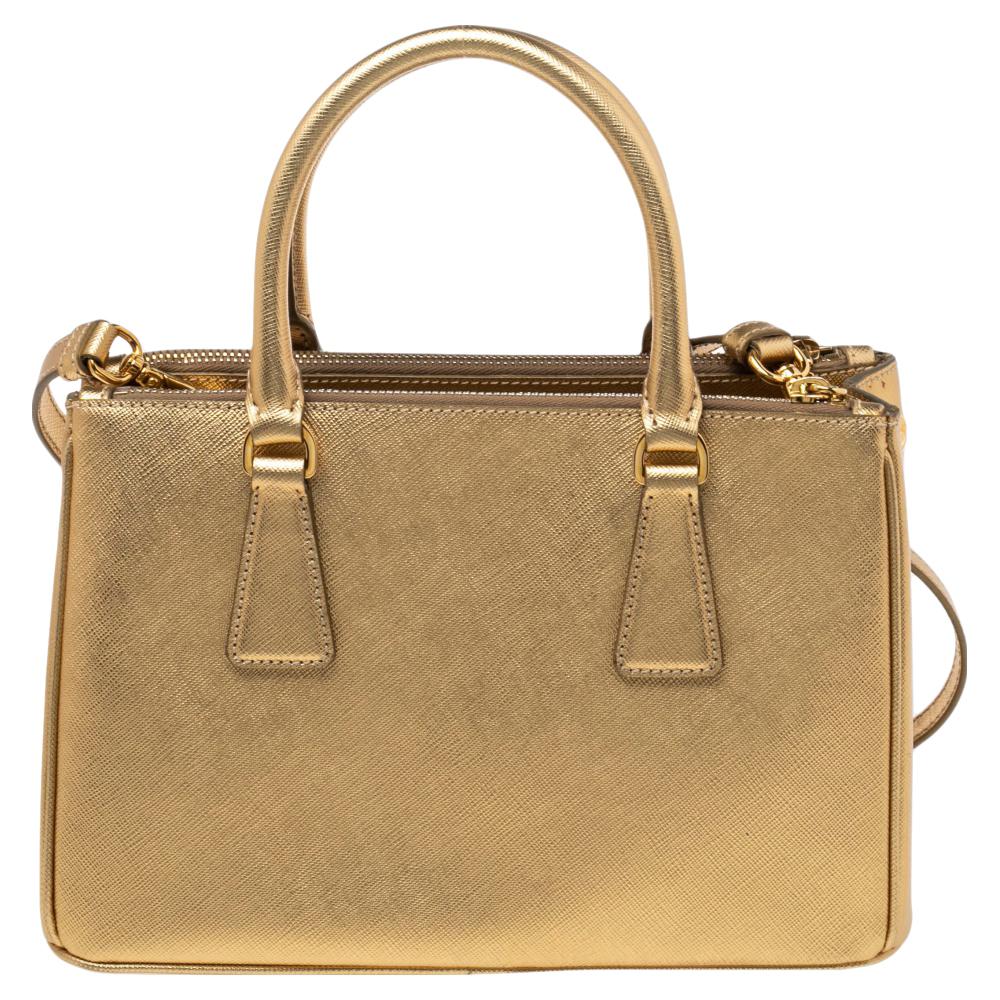 Feminine in shape and grand in design, this Double Zip tote by Prada will be a loved addition to your closet. It has been crafted from Saffiano Lux leather and styled minimally with gold-tone hardware. It comes with two top handles, two zip