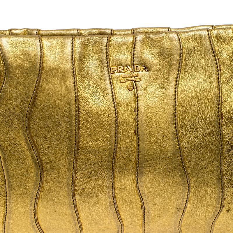A stunning creation, this Prada clutch is a must have! Its leather exterior is given an exotic look with metallic gold hue and an interesting wave pattern. It has a top zip closure and the gold-tone brand logo at the front. Lined with satin on the