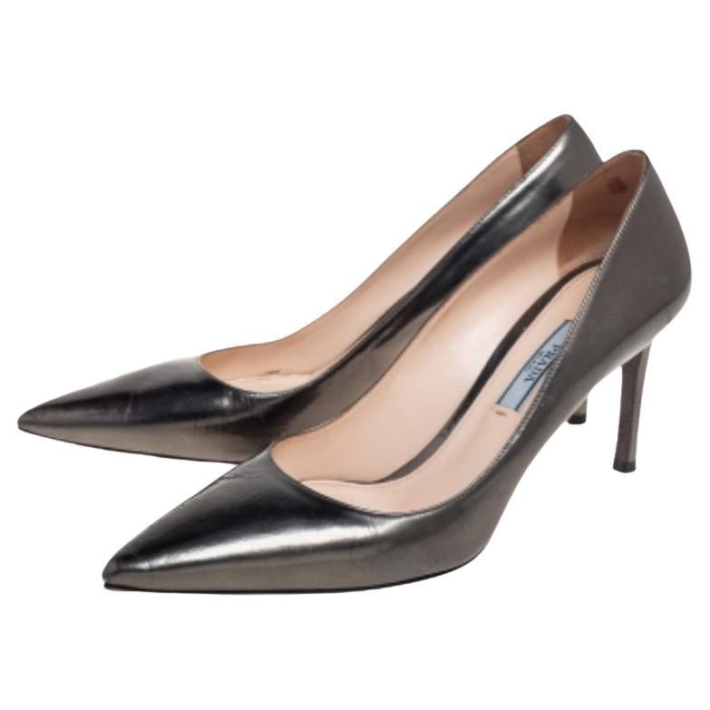 La silhouette élégante et pointue en gris métallisé confère à cette paire d'escarpins Prada un attrait élevé. Conçue en cuir, elle arbore des ferrures dorées et des semelles de marque. Les talons de 8 cm de ces chaussures garantissent un équilibre