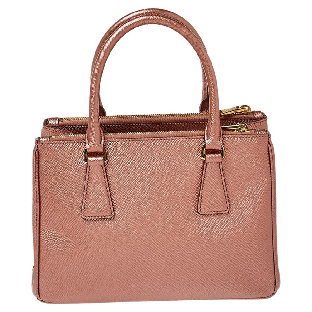 Loved for its classic appeal and functional design, Galleria is one of the most iconic and popular bags from the house of Prada. This beauty in metallic pink is crafted from leather and is equipped with two top handles, the brand logo at the front