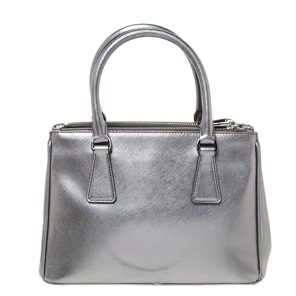 Feminine in shape and grand on design, this Double Zip tote by Prada will be a loved addition to your closet. It has been crafted from metallic silver leather and styled minimally with silver-tone hardware. It comes with two top handles, two zip