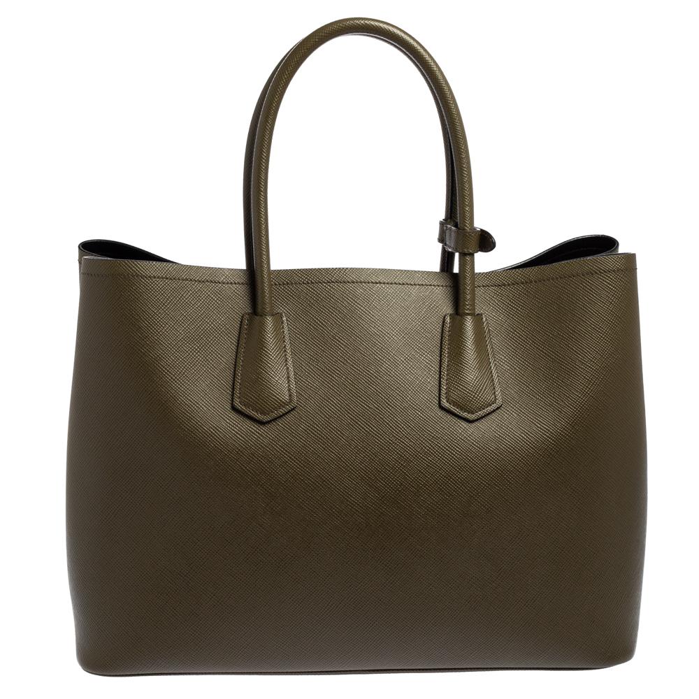 This elegant tote from Prada is crafted from Saffiano Cuir leather and is perfect for daily use. The bag features double handles, a leather tag, and protective metal feet at the bottom. The leather-lined interior houses two open compartments and is