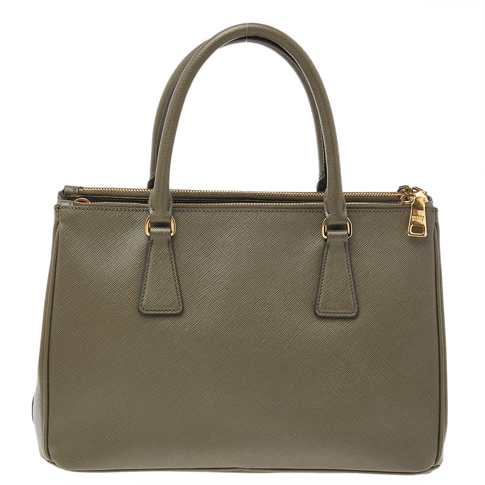 Feminine in shape and grand on design, this Double Zip tote by Prada will be a loved addition to your closet. It has been crafted from Saffiano leather and styled minimally with gold-tone hardware. It comes with two top handles, two zip