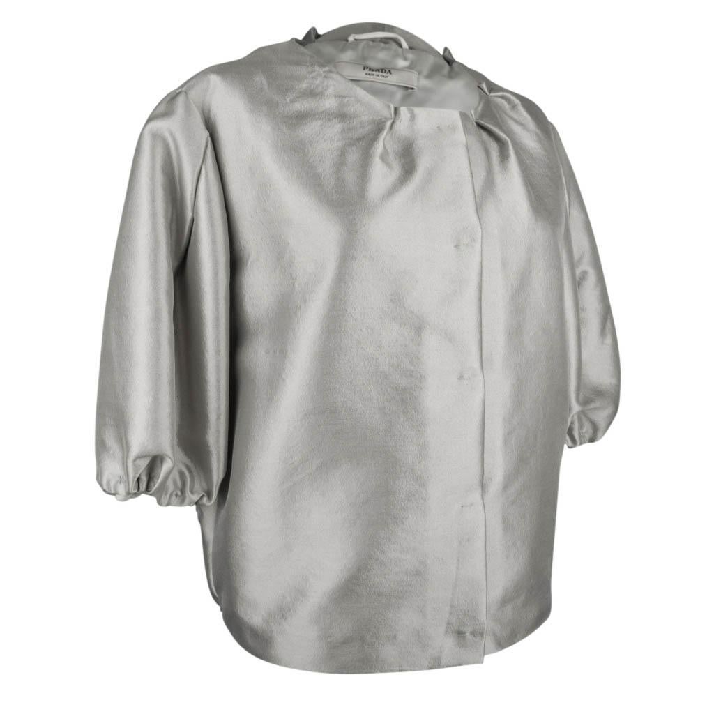 Guaranteed authentic Prada amazing jacket that has real Jackie O - Audrey Hepburn style!  
Highly styled silver gray jacket.
No collar the neck line is accentuated with small 'catches' with a single stitch.
The sleeves end below the elbow in a