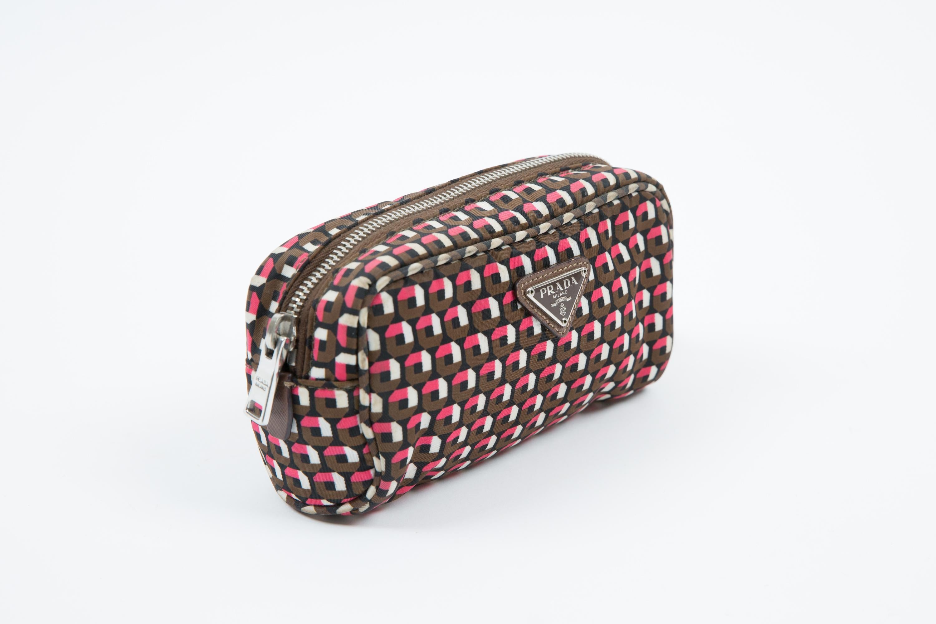 Pochette en nylon imprimé géométrique multicolore avec logo triangulaire en métal émaillé sur le devant, bracelet amovible en cuir Saffiano marron, doublure en nylon monogramme noir avec poche zippée, fermeture zippée sur le dessus et accessoires en