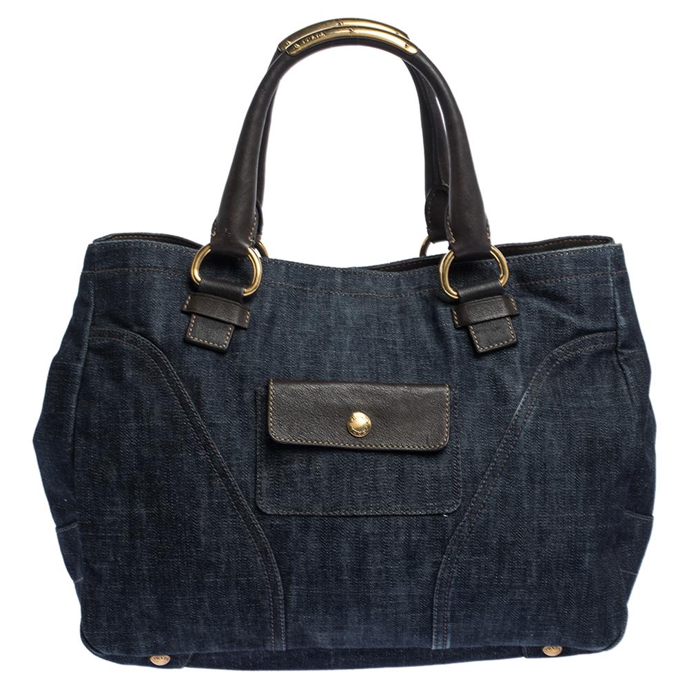 Be the talk of the town when you carry this Prada handbag. Look fabulous with this navy blue denim and leather bag. It has dual handles, chain & zip detailing, gold-tone hardware, and brand logo in the front. Stow all your belongings inside the