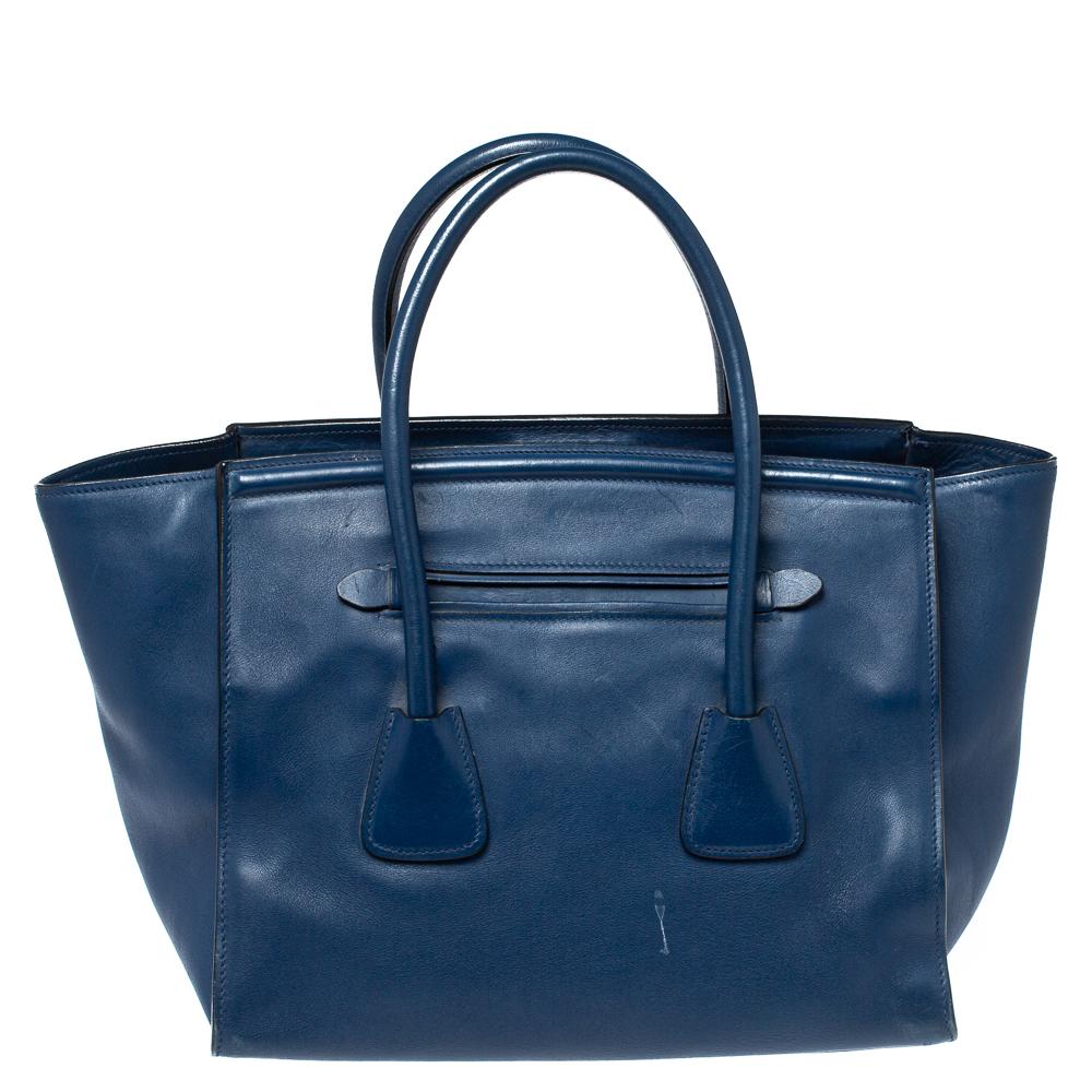 Feminine in shape and grand on design, this tote by Prada will be a loved addition to your closet. It has been crafted from navy blue leather and styled minimally with gold-tone hardware. It comes with two top handles, a front zip pocket, winged