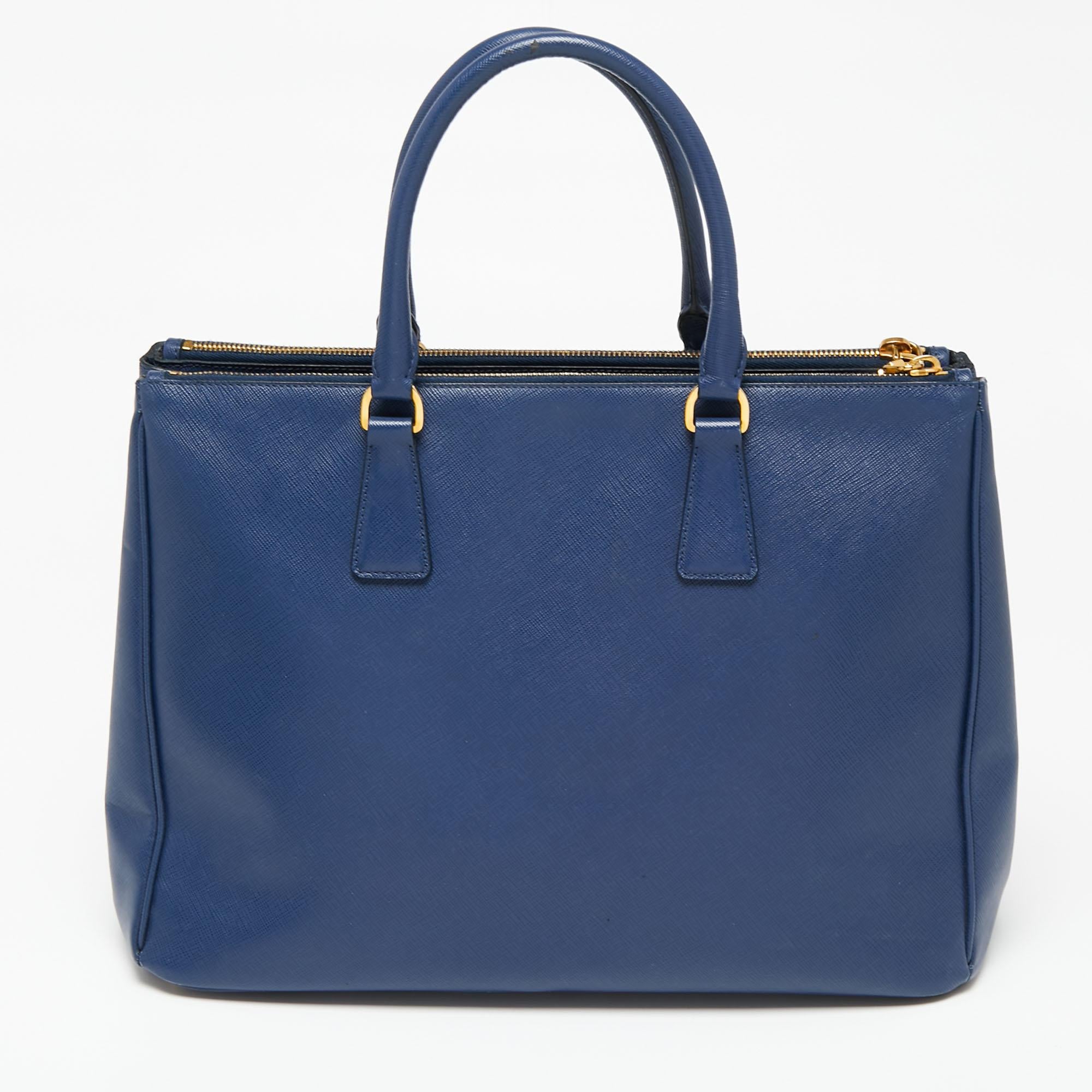 Loved for its classic appeal and functional design, Galleria is one of the most iconic and popular bags from the house of Prada. This beauty in navy blue is crafted from Saffiano Lux leather and is equipped with two top handles, the brand logo on