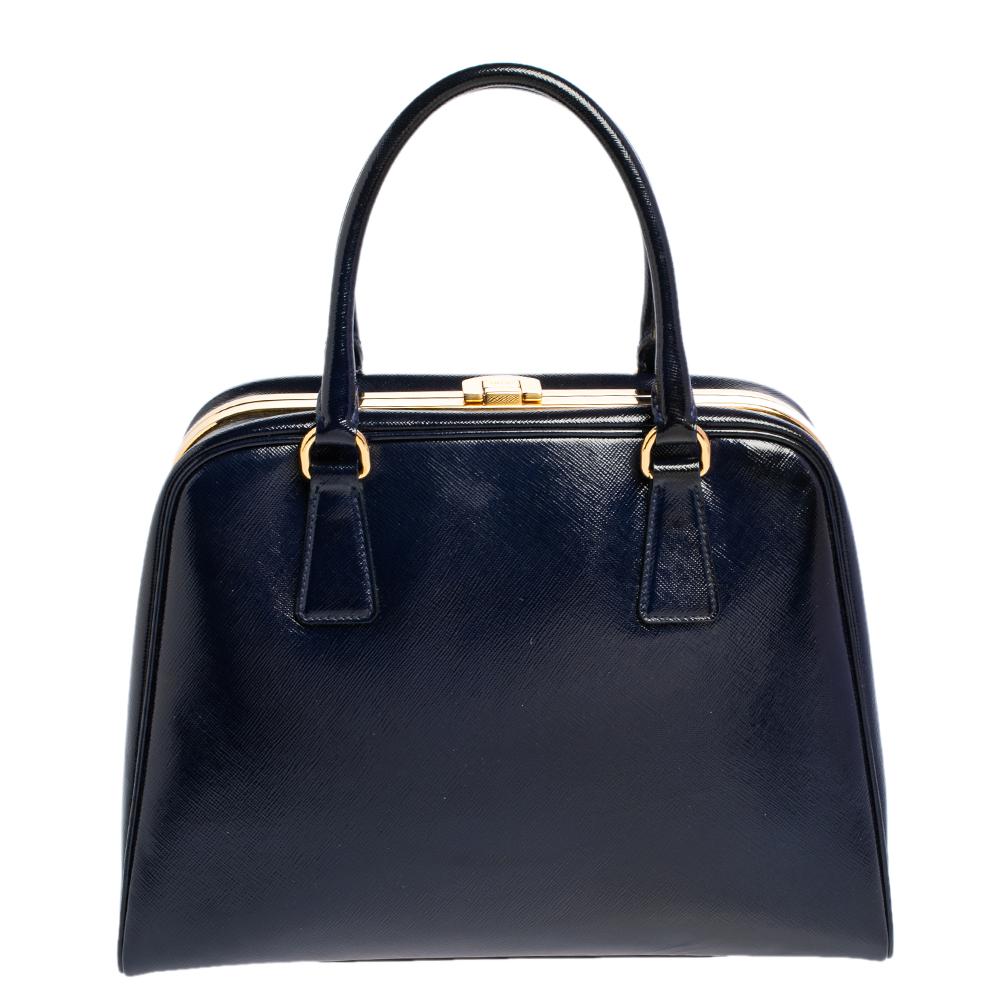 High in appeal and style, this satchel is a Prada creation. It has been crafted from Saffiano patent leather and shaped to exude class and luxury. The bag is designed with a gold-tone clasp on the top metal frame and comes with two handles and a