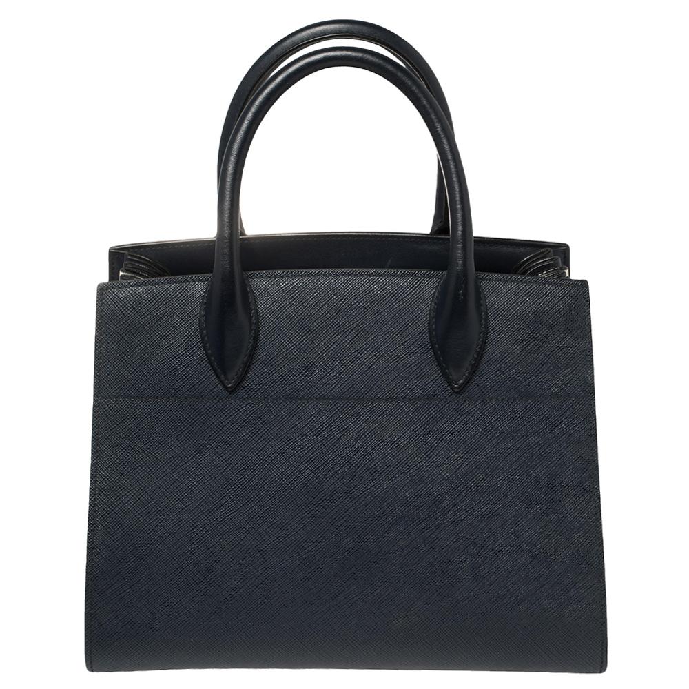 Feminine and stylish, this Bibliotheque tote from Prada is a worthy buy. Crafted from navy blue and white leather, the bag features dual top handles, a removable shoulder strap, and protective metal feet at the bottom. The leather-lined interior is