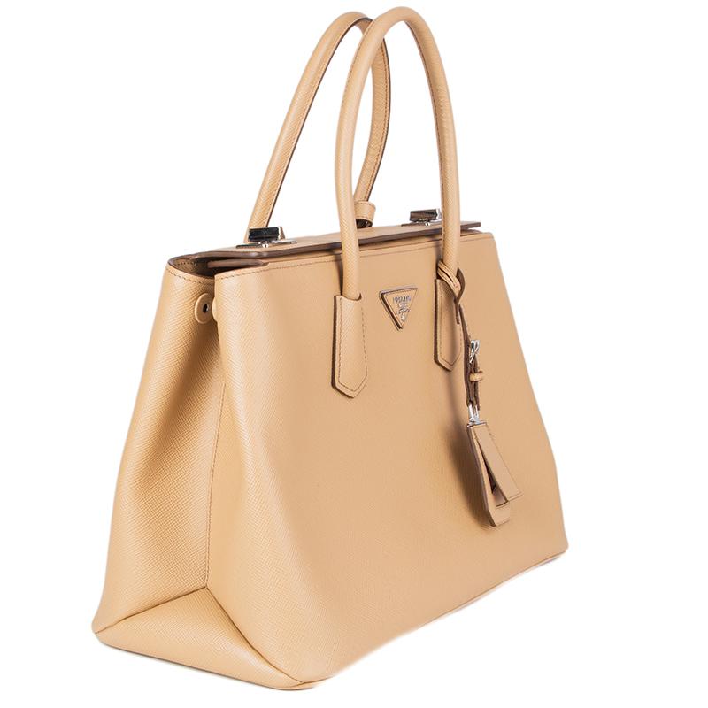 Prada 'Twin Tote' in noisette (beige) Saffiano leather. Featuring tubular tote handles with strap keeper and hanging buckled luggage tag. Opens with double turn-locks secure folded top and is lined in orange lambskin with a big center zip