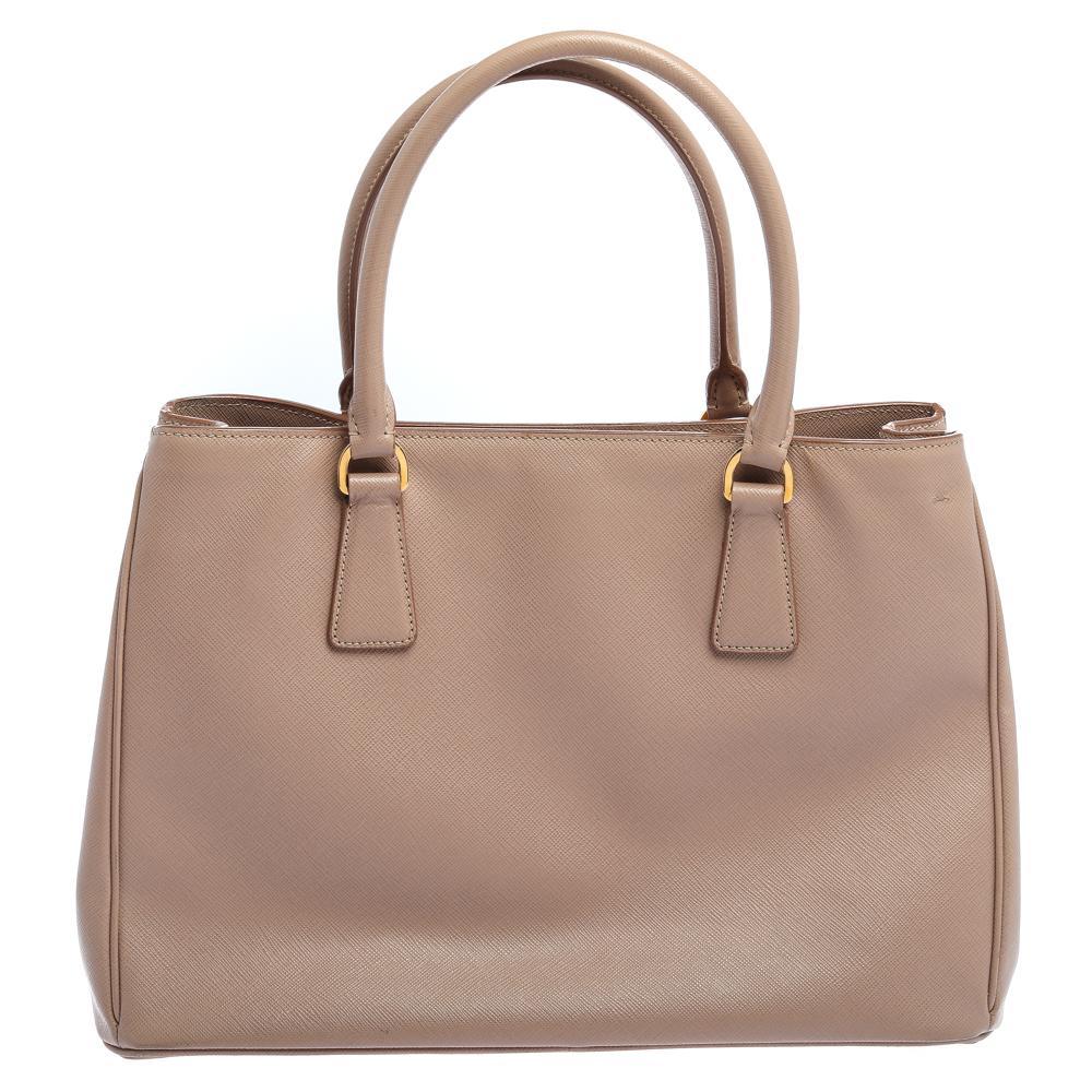 Feminine in shape and grand on design, this Zip tote by Prada will be a loved addition to your closet. It has been crafted from Saffiano Lux leather and styled minimally with gold-tone hardware. It comes with two top handles and a nylon-lined