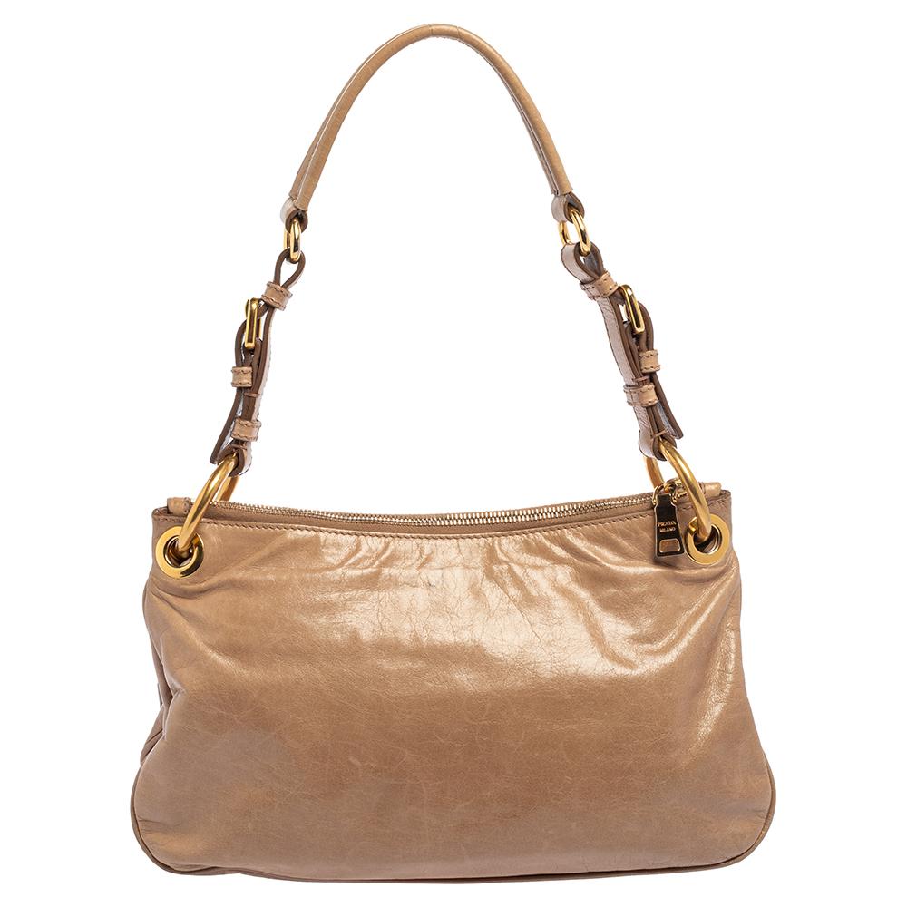 This Prada hobo is everything you need to elevate your daily ensembles. Crafted from Vitello Shine leather, it comes in a nude beige hue that is versatile. With a spacious nylon interior, this bag is designed to hold essentials. It is finished with