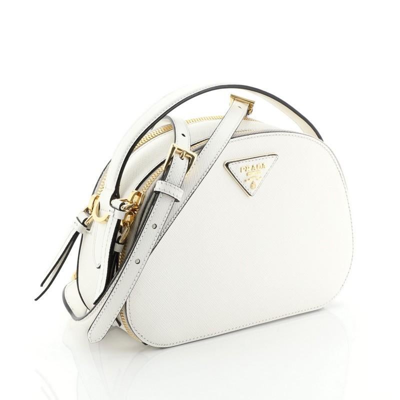 This Prada Odette Top Handle Bag Saffiano Leather Small, crafted in white leather, features a leather top handle and gold-tone hardware. Its two-compartment zip closures open to a black fabric interior. 

Estimated Retail Price: $1,950
Condition: