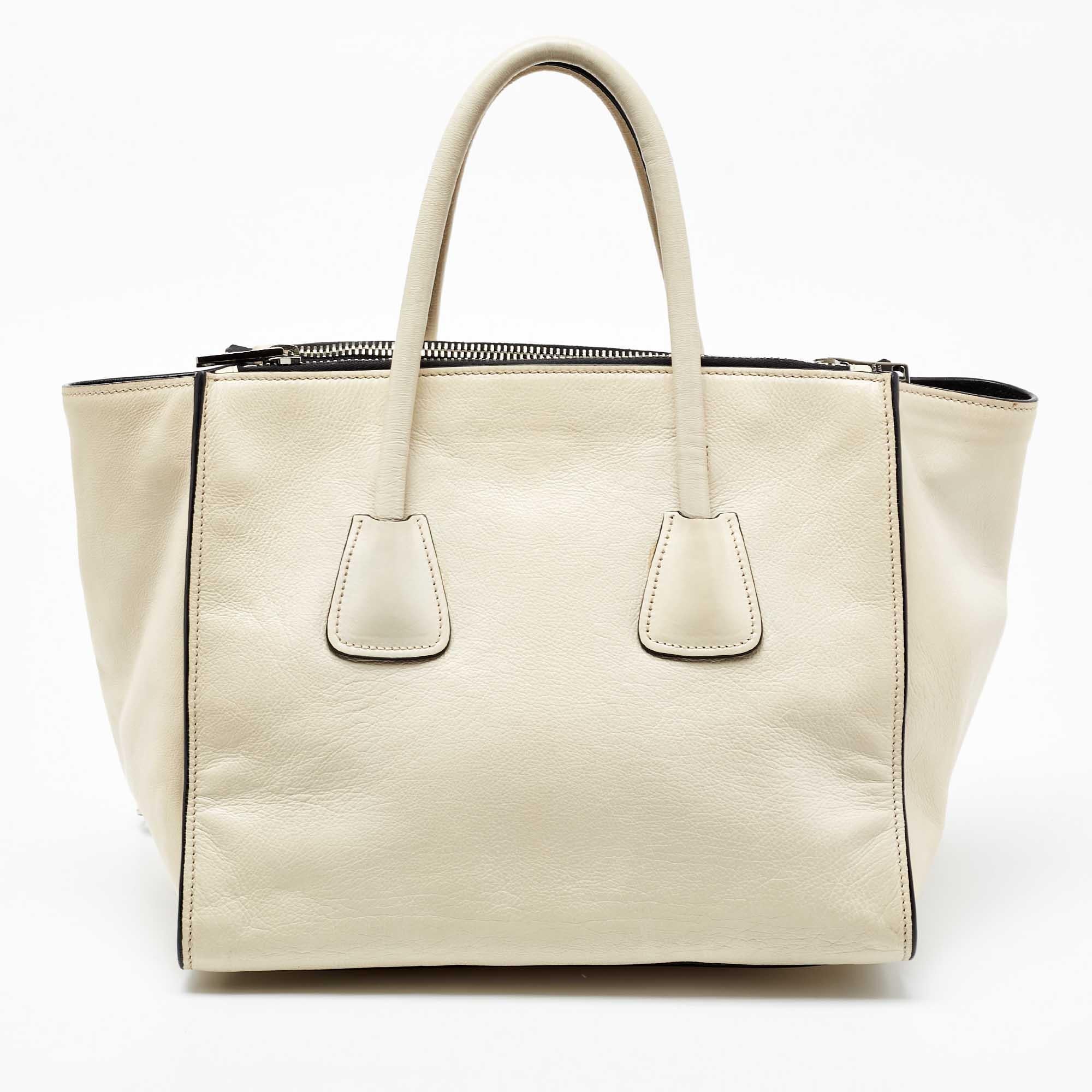 This lovely tote from Prada is crafted from leather and features an off-white shade. It flaunts dual round handles, a detachable strap, protective metal feet, and a spacious nylon-lined interior. Perfect for work and after.

Includes; Original