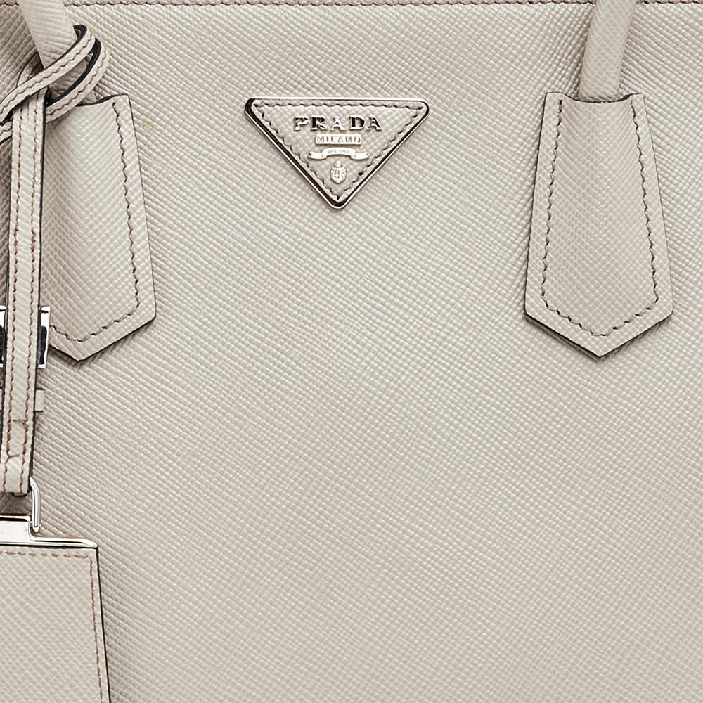 Stay on top of your fashion game with this Twin tote from Prada! Crafted from Saffiano Cuir leather, the tote has a soft hue, two rolled handles, a leather tag, and protective metal feet. The insides are lined and sized to dutifully carry your