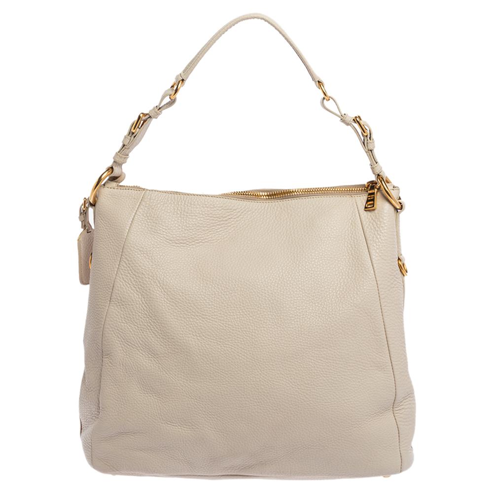 Flaunt this fantastic-looking hobo from Prada and give yourself a sophisticated look. The bag is held by a single handle and crafted from off-white hued leather. It comes with a nylon-lined interior that is secured by a zip. The hobo also features a
