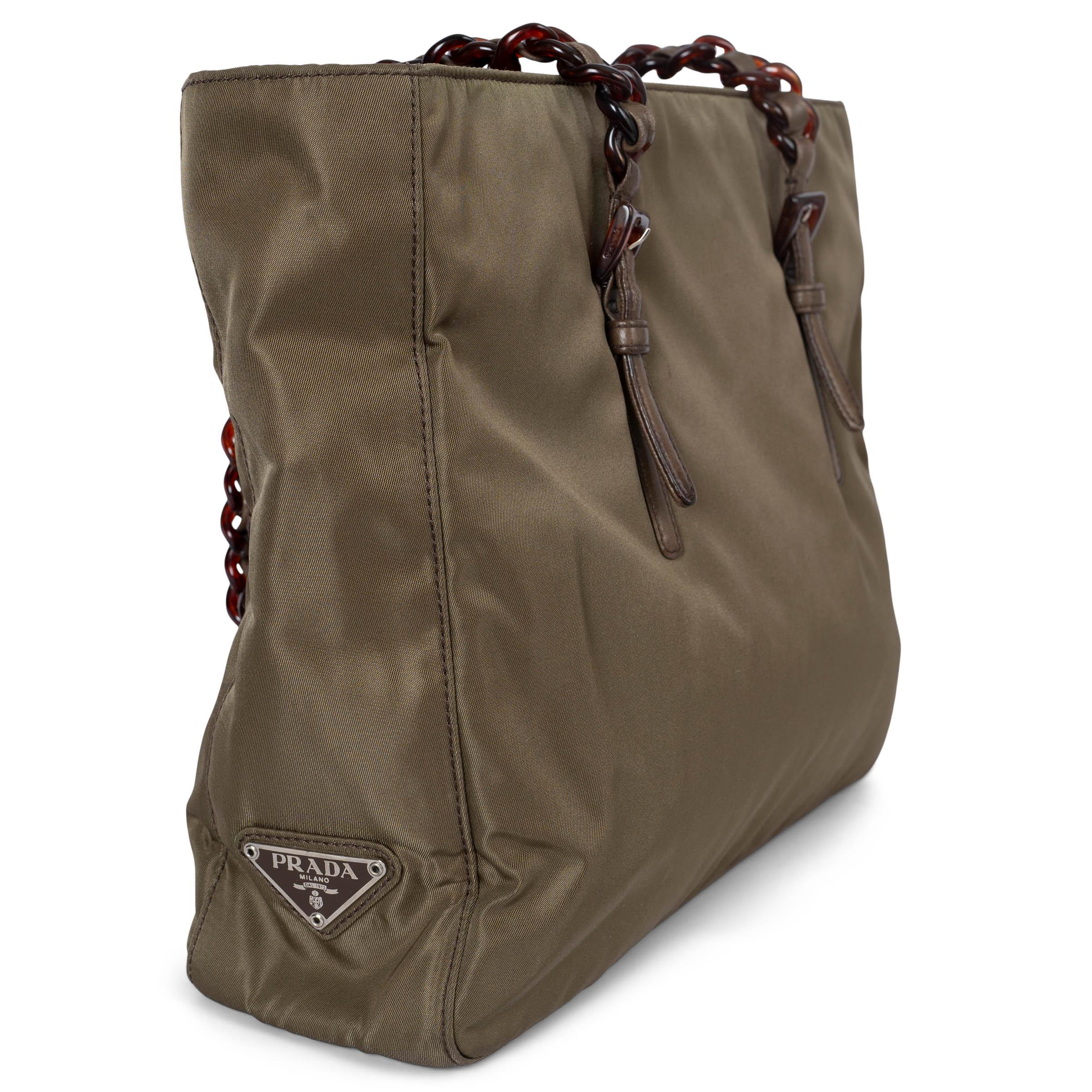 This 100% authentic Prada tote is crafted from olive green nylon and features matching olive green leather trims for a sleek and durable design. The bag is accented with faux tortoise chain straps and the iconic enamel triangle logo patch. It closes
